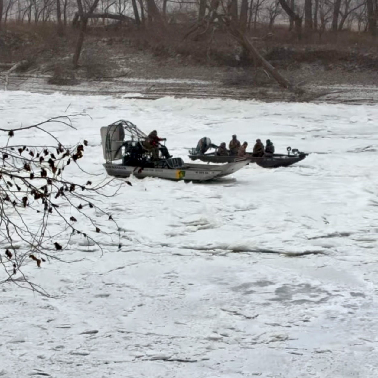 An airboat rescuing a jon boat from a frozen river.