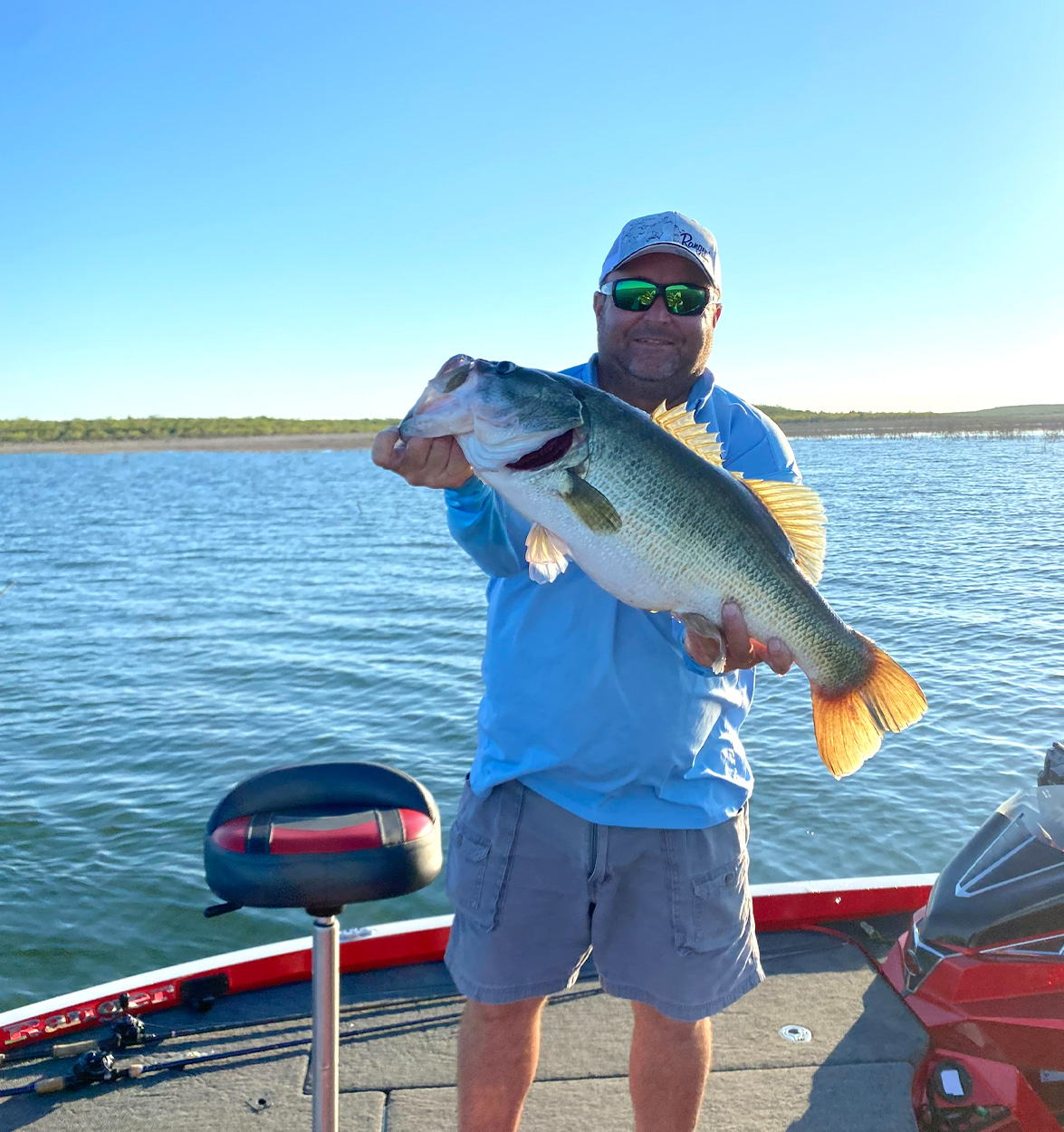 A bass fisherman holds up a largemouth on a boat.