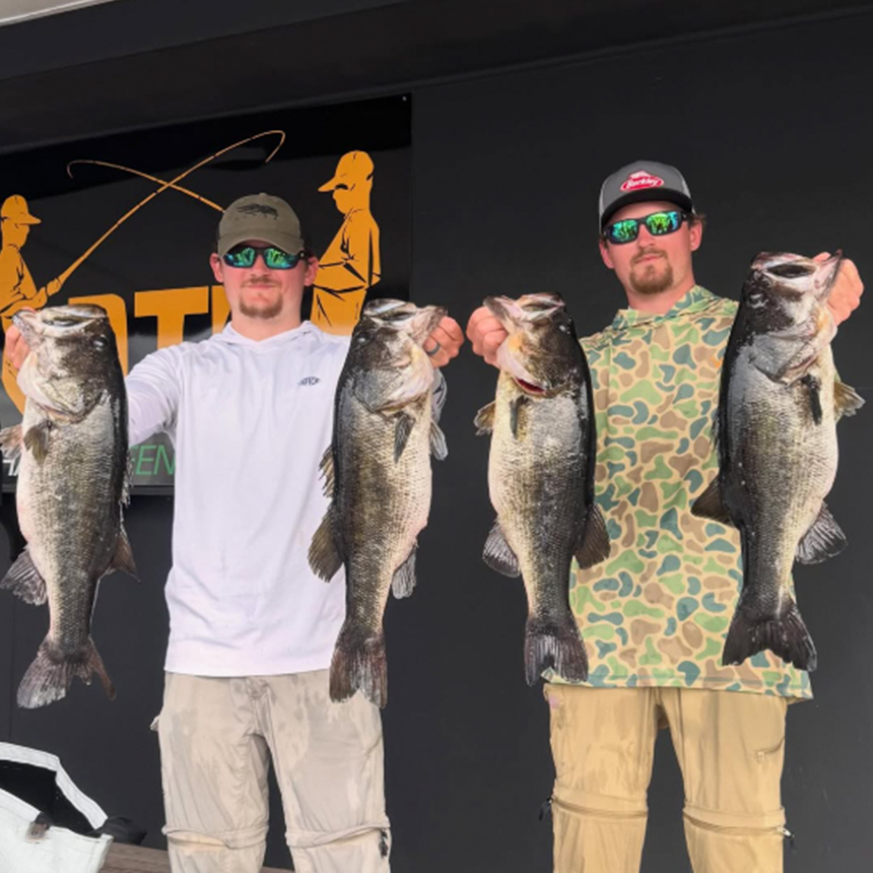 Two anglers hold up bass at a tournament. 