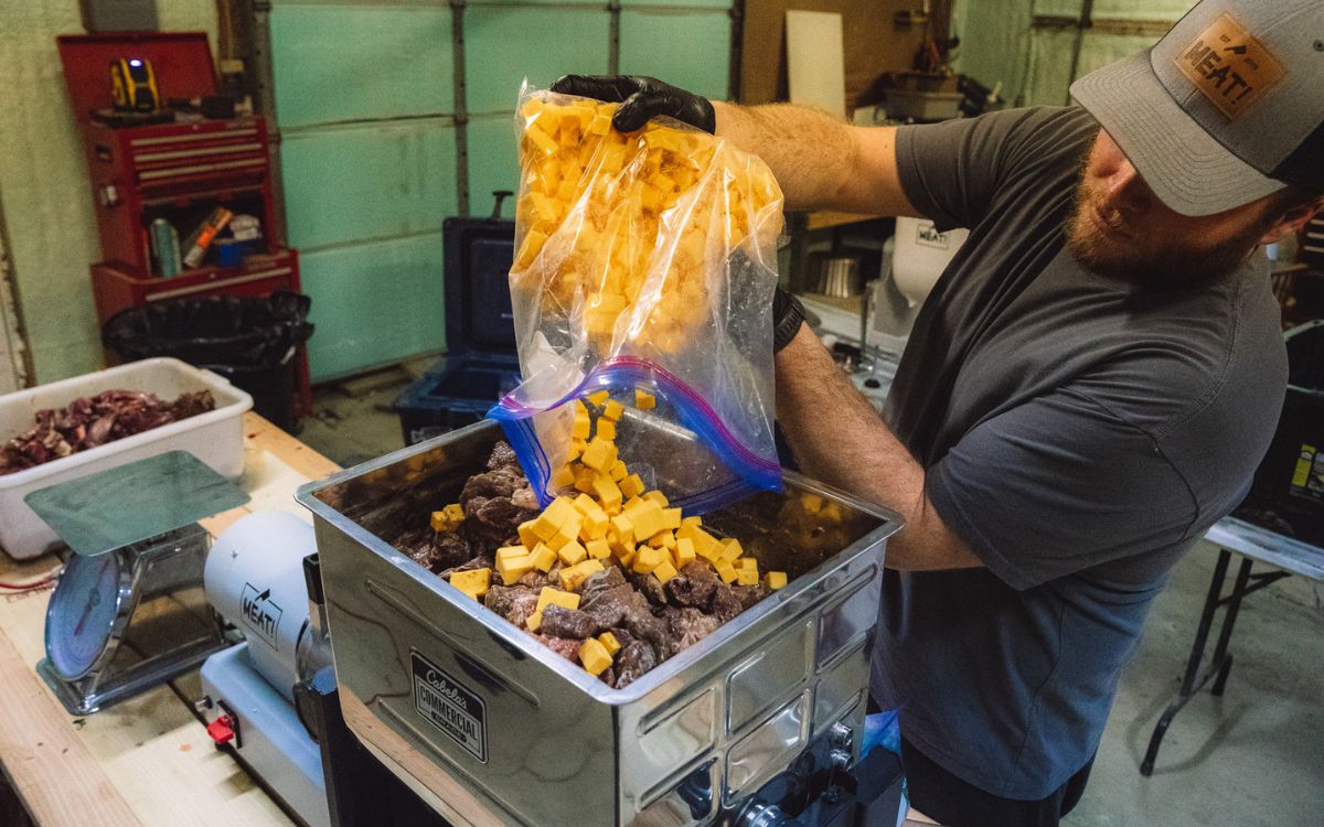 A man dumps cheese into a mixer containing venison and pork.