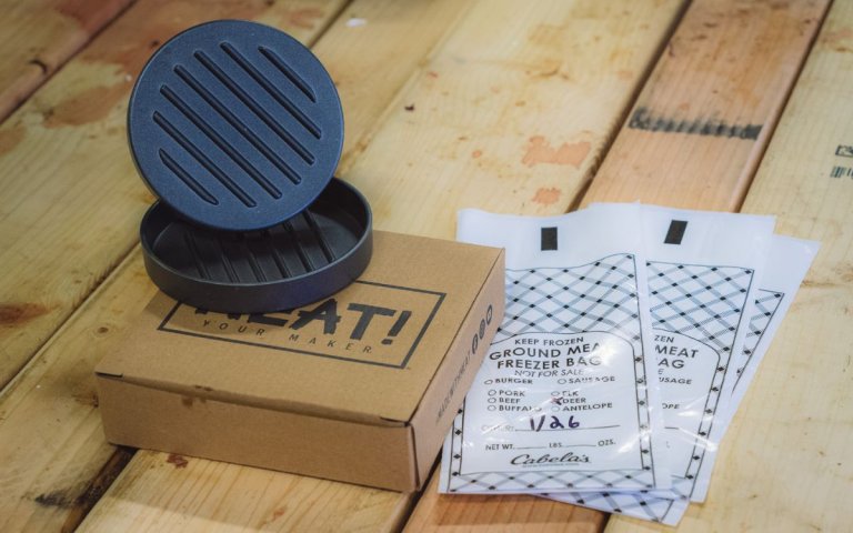 A burger press sits on display next to empty burger bags.