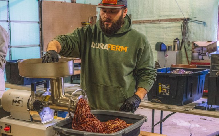 A man puts meat through a grinder.