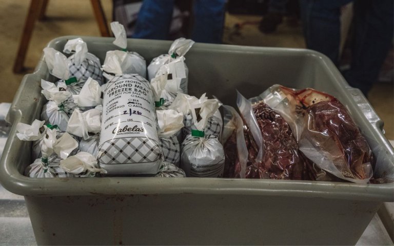 A meat lug full of packaged burger and pastrami sits on a table.