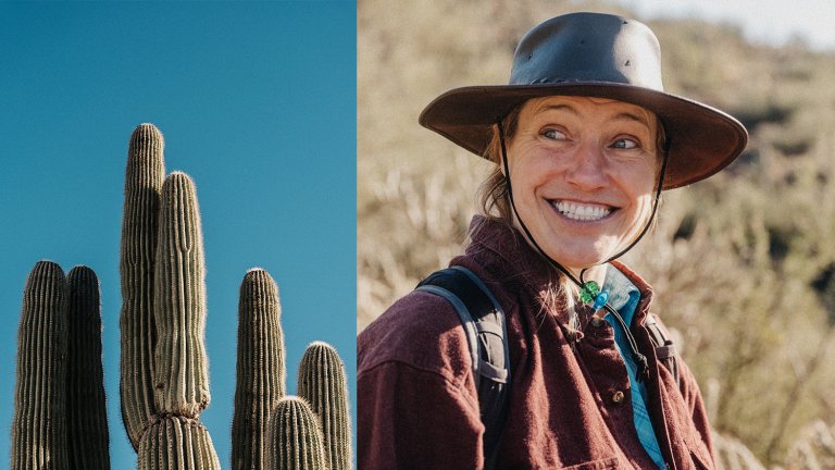 A portrait of a smiling woman with a big leather hat beside a cactus against a blue sky