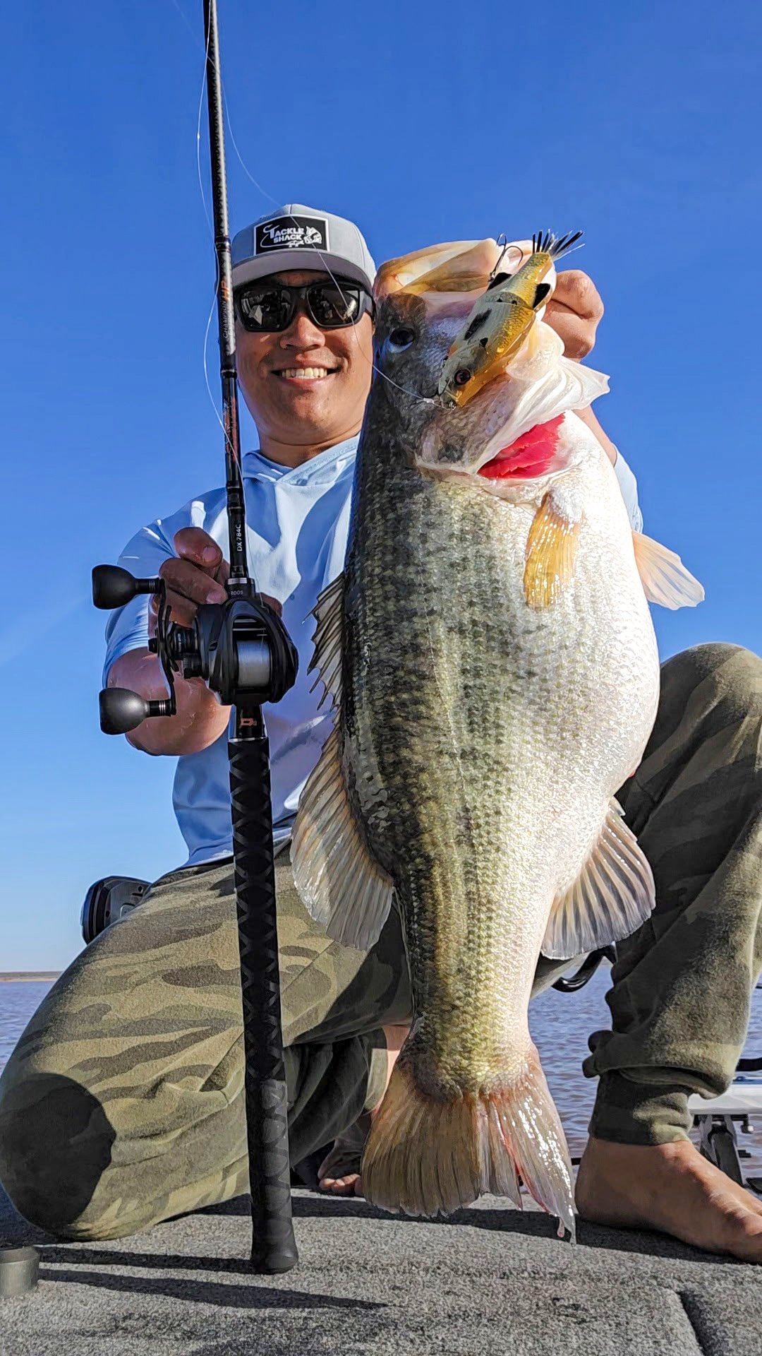 A fisherman holds up a 13-pound bass on a boat.