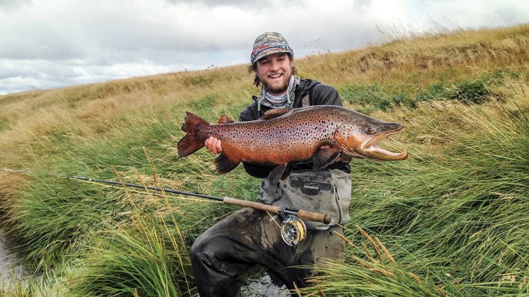 A man holds up a huge brown trout.