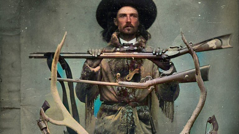 American folk hero Buffalo Bill Cody poses with taxidermy deer, antlers, and revolvers against a backdrop, 1871. Note: Image has been digitally colorized using a modern process.