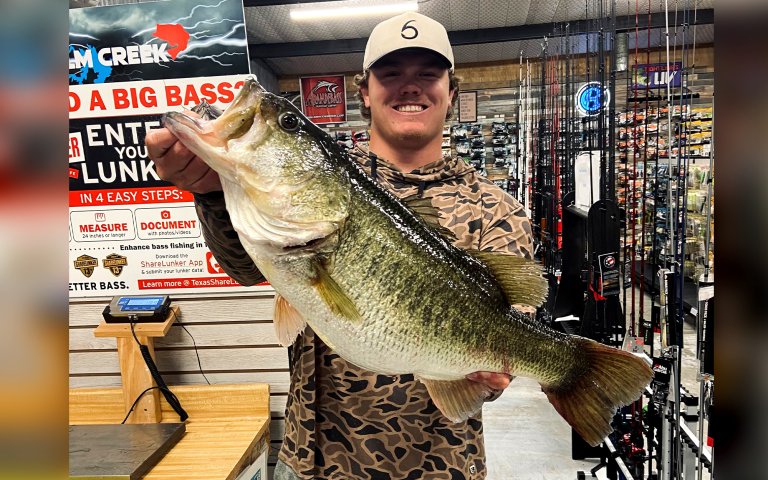 A bass angler holds up a huge largemouth at a marina.