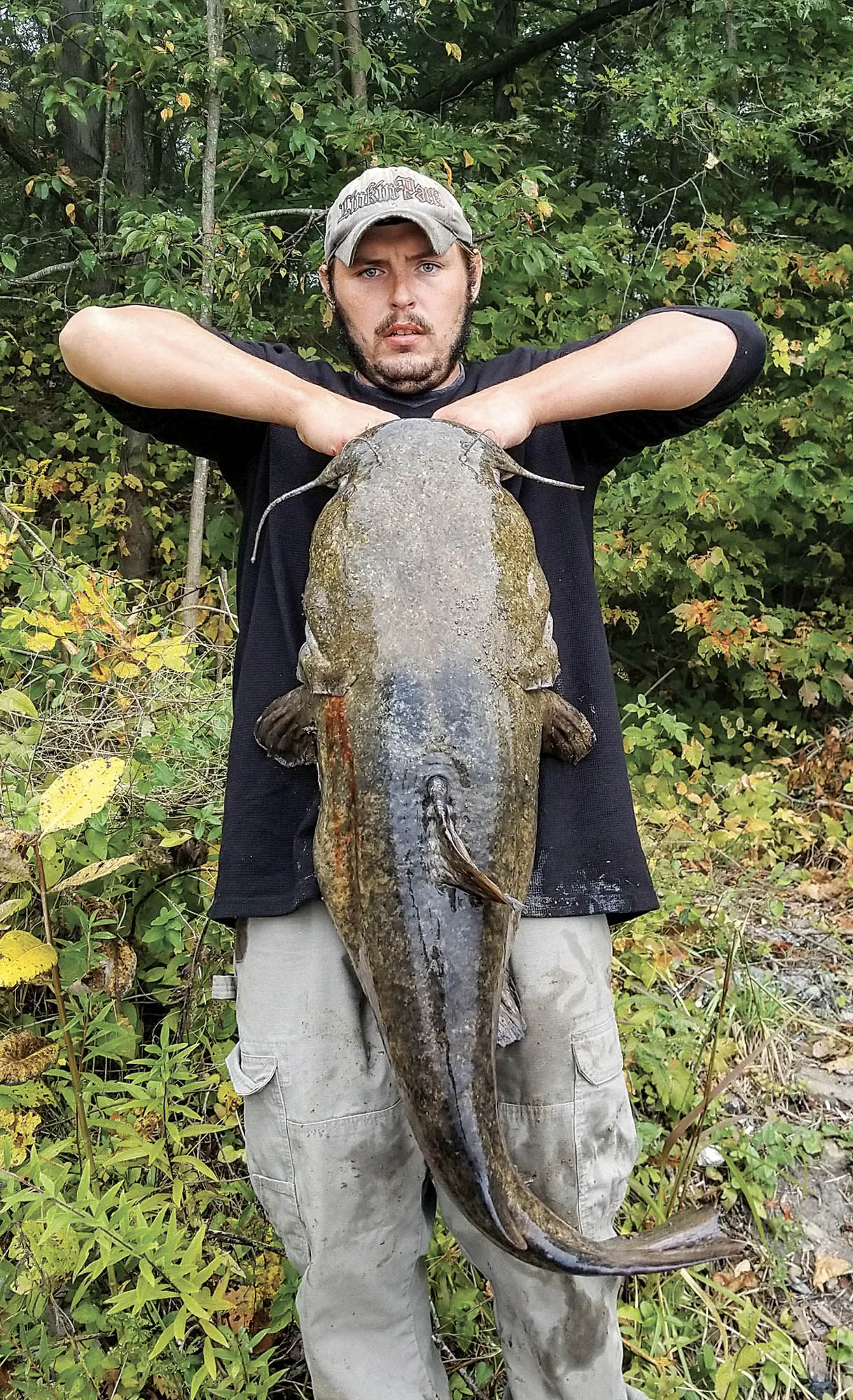 A man holds up a big flathead catfish.