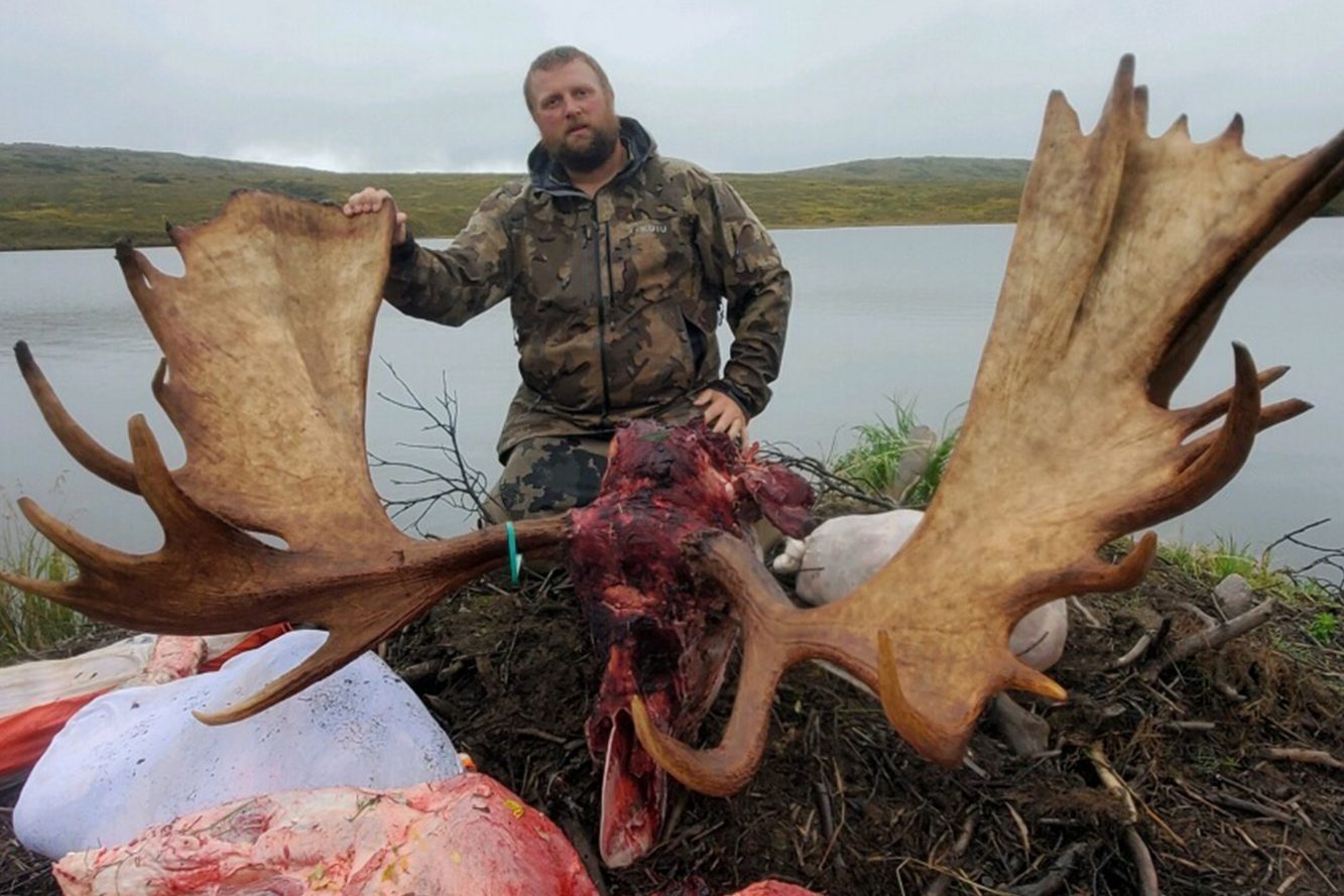 hunter with moose rack and meat at edge of lake