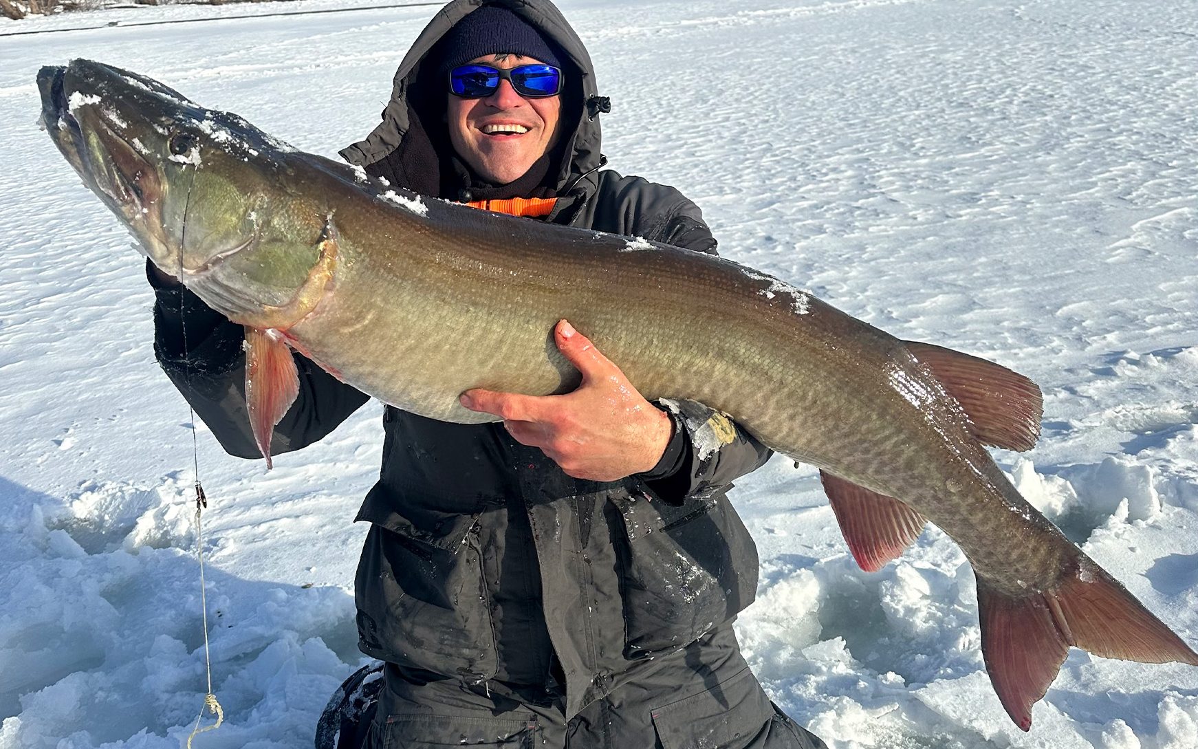 An angler with a record-sized muskie caught through the ice.