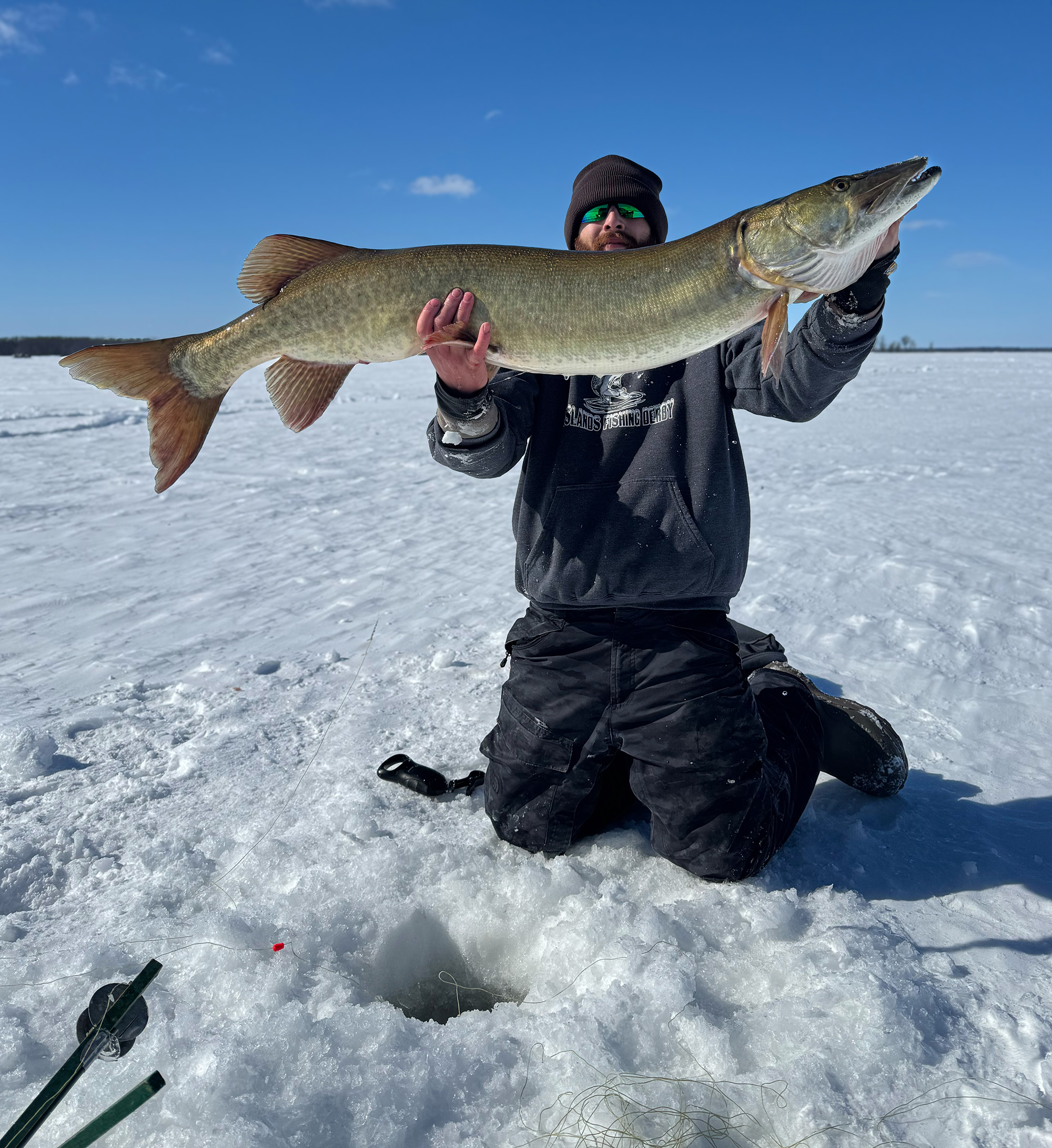 An angler holds up a huge Vermont muskie caught through the ice.