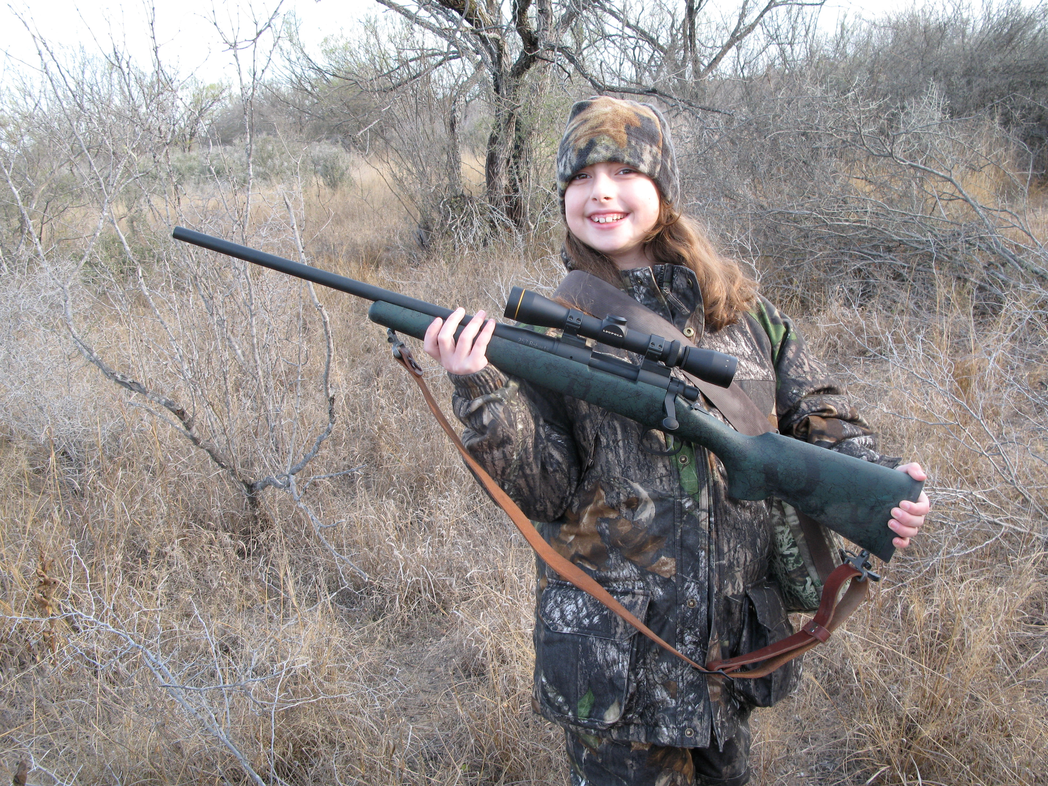 A young hunter holding a 25 caliber rifle in Texas brush country.
