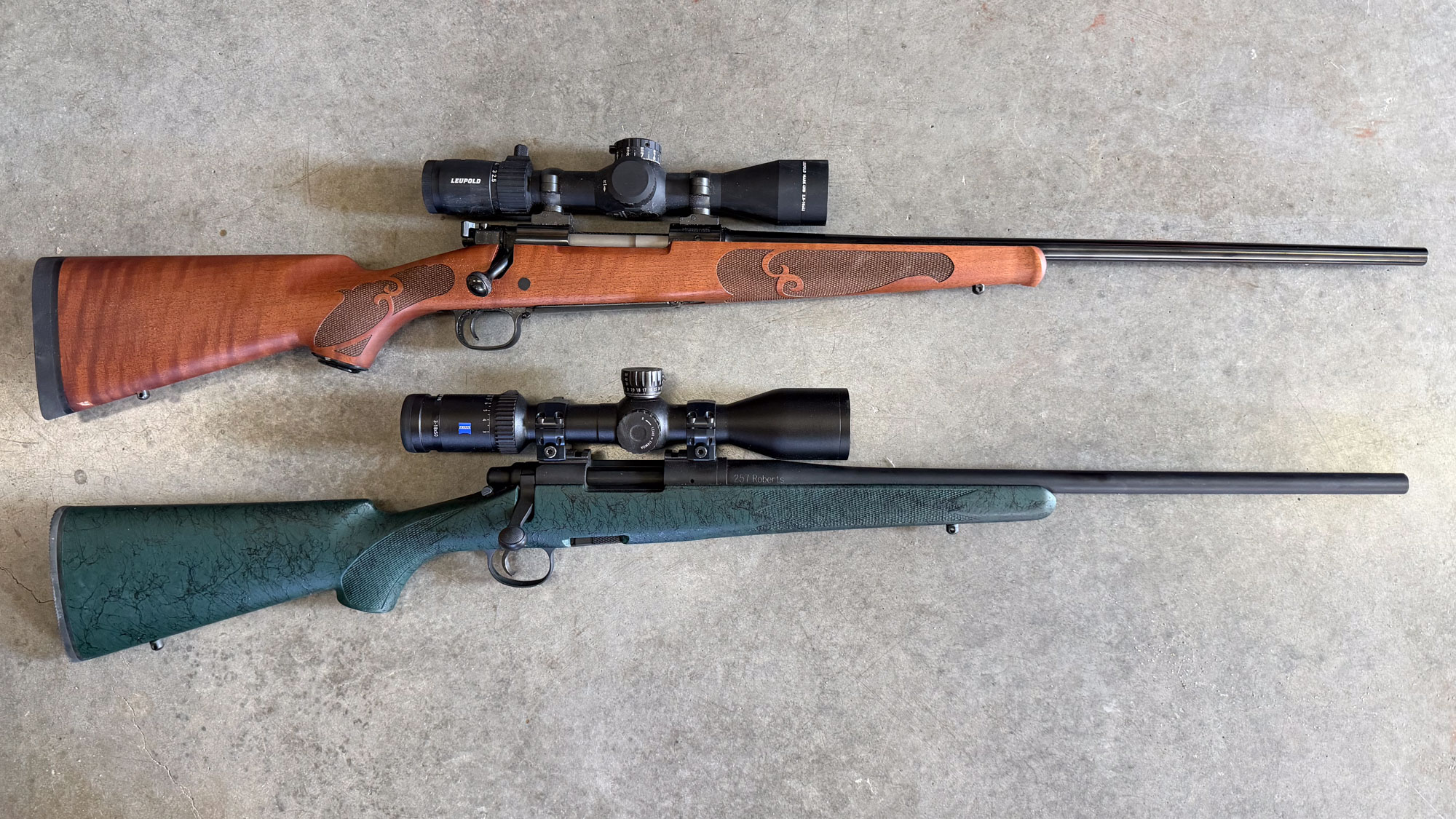 Two bolt action 25 caliber rifles photographed on concrete.