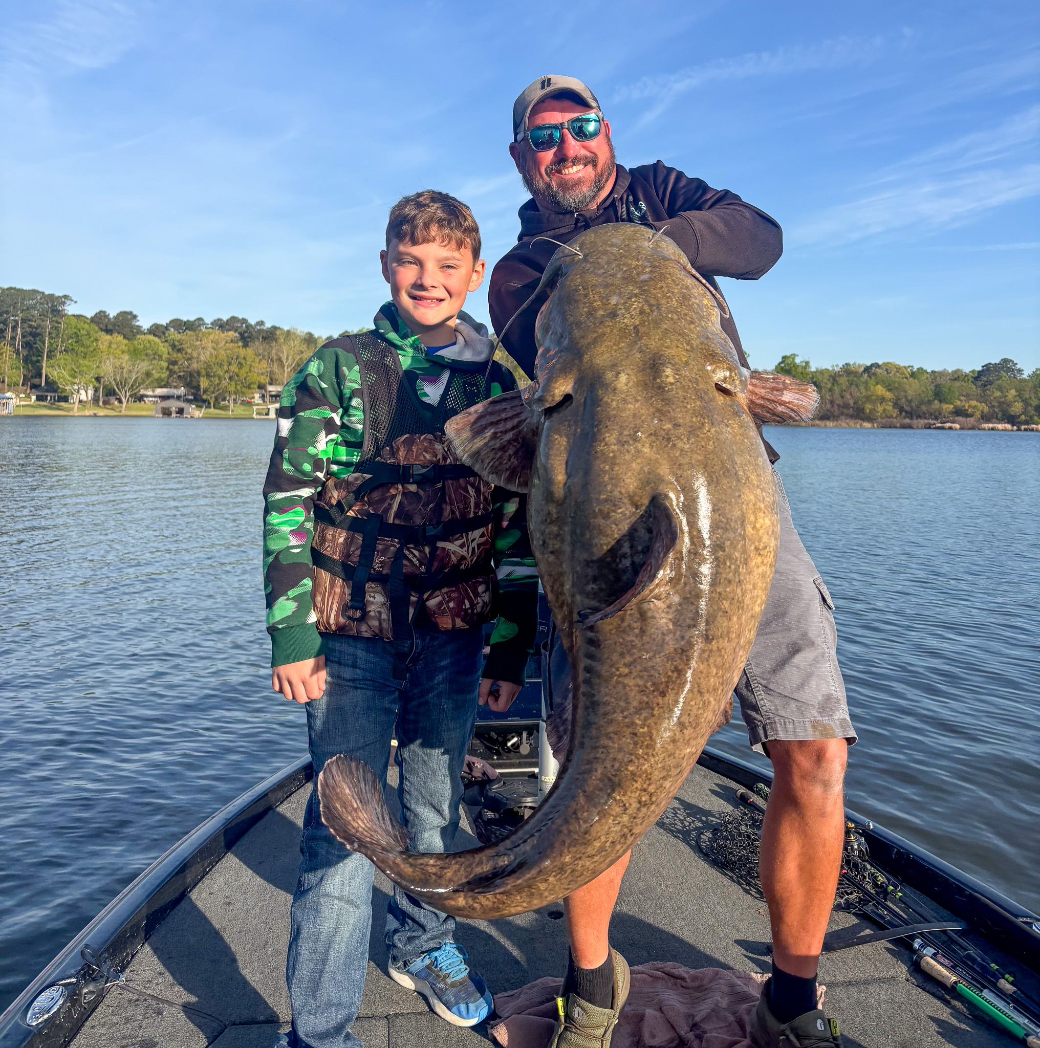 A man holds up a big flathead on a boat.