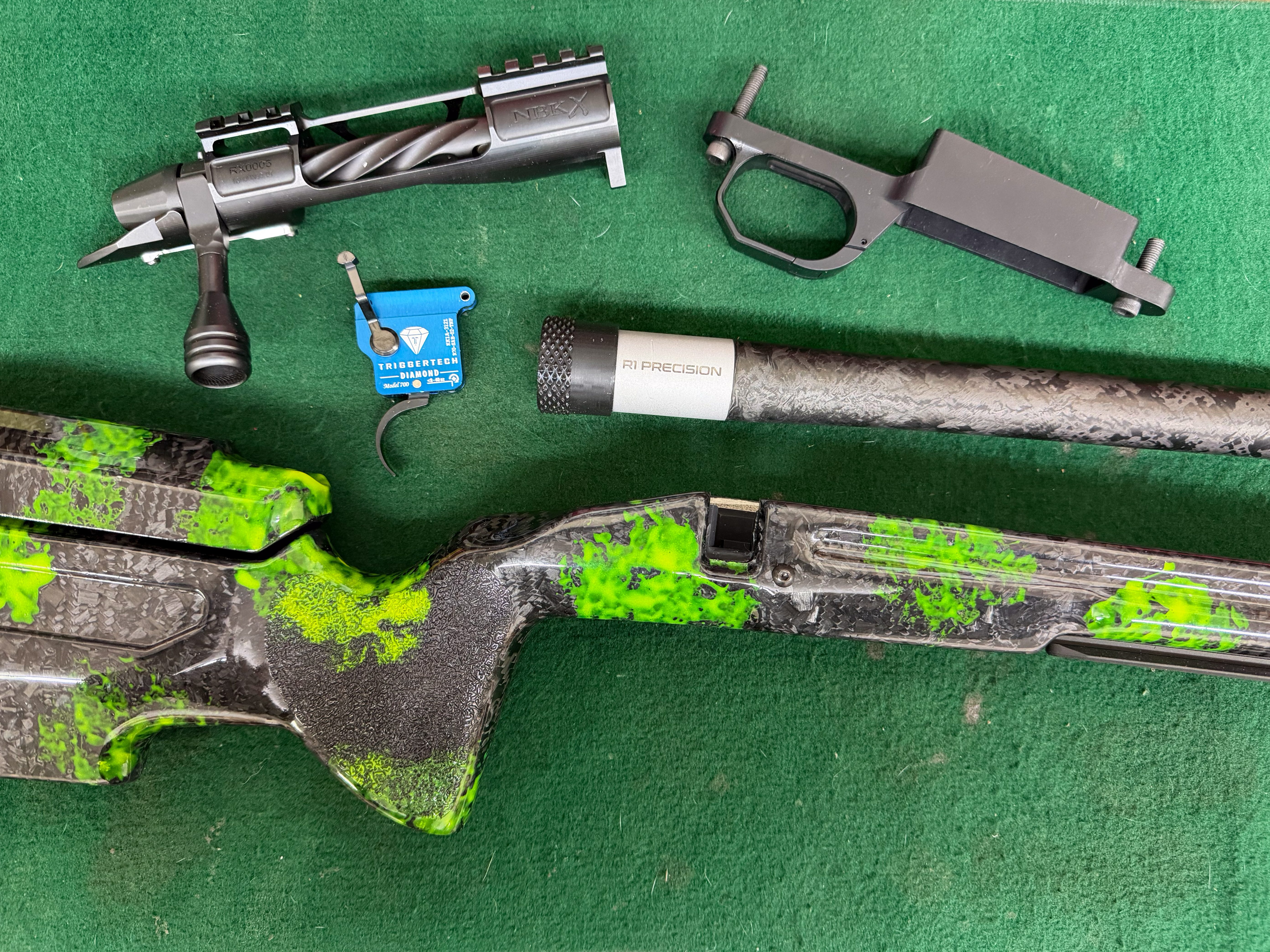 A custom 25 caliber rifle spread out on green felt with an action and triggertech diamond trigger.