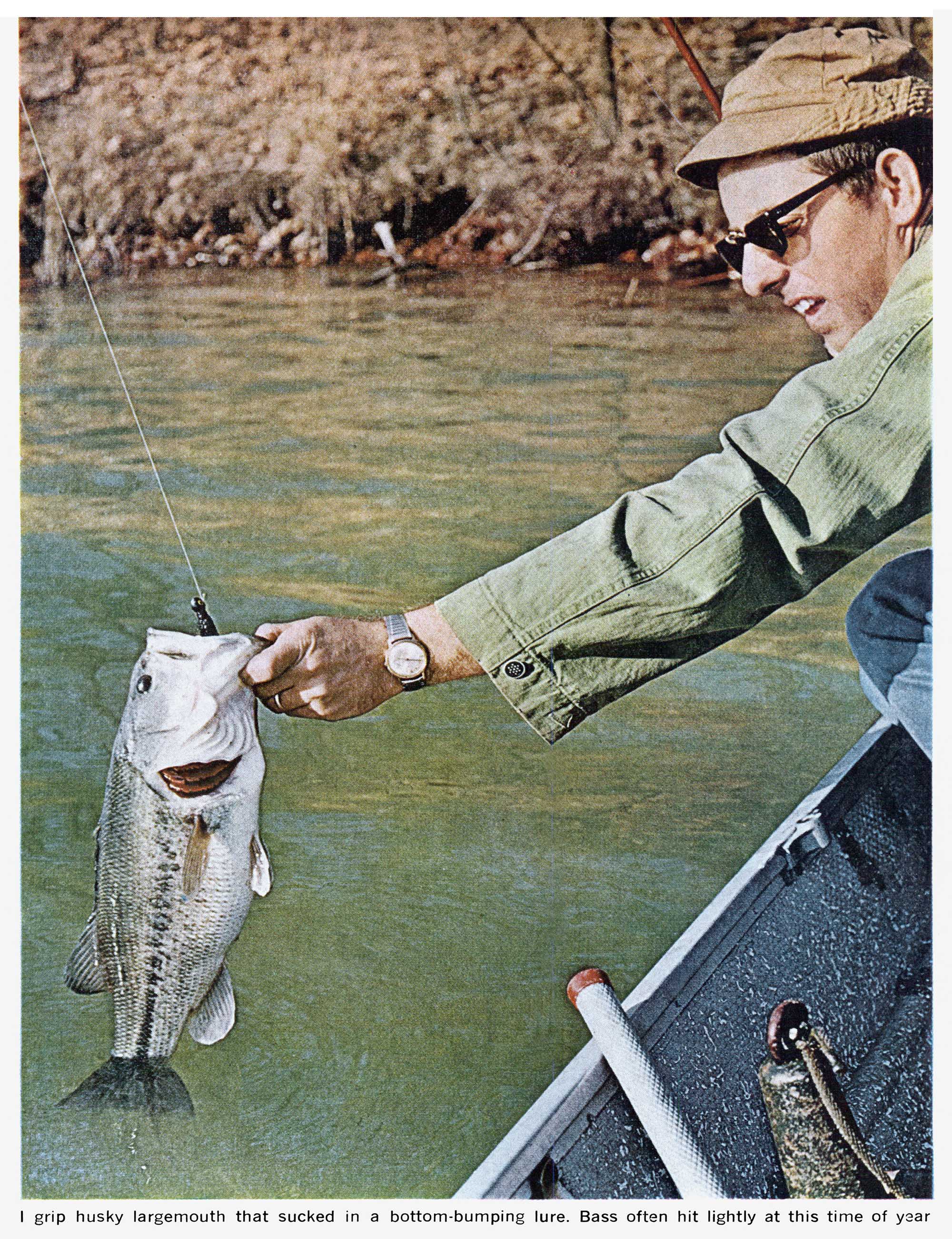 A man picking up a bass from the side of a boat in an old photo.