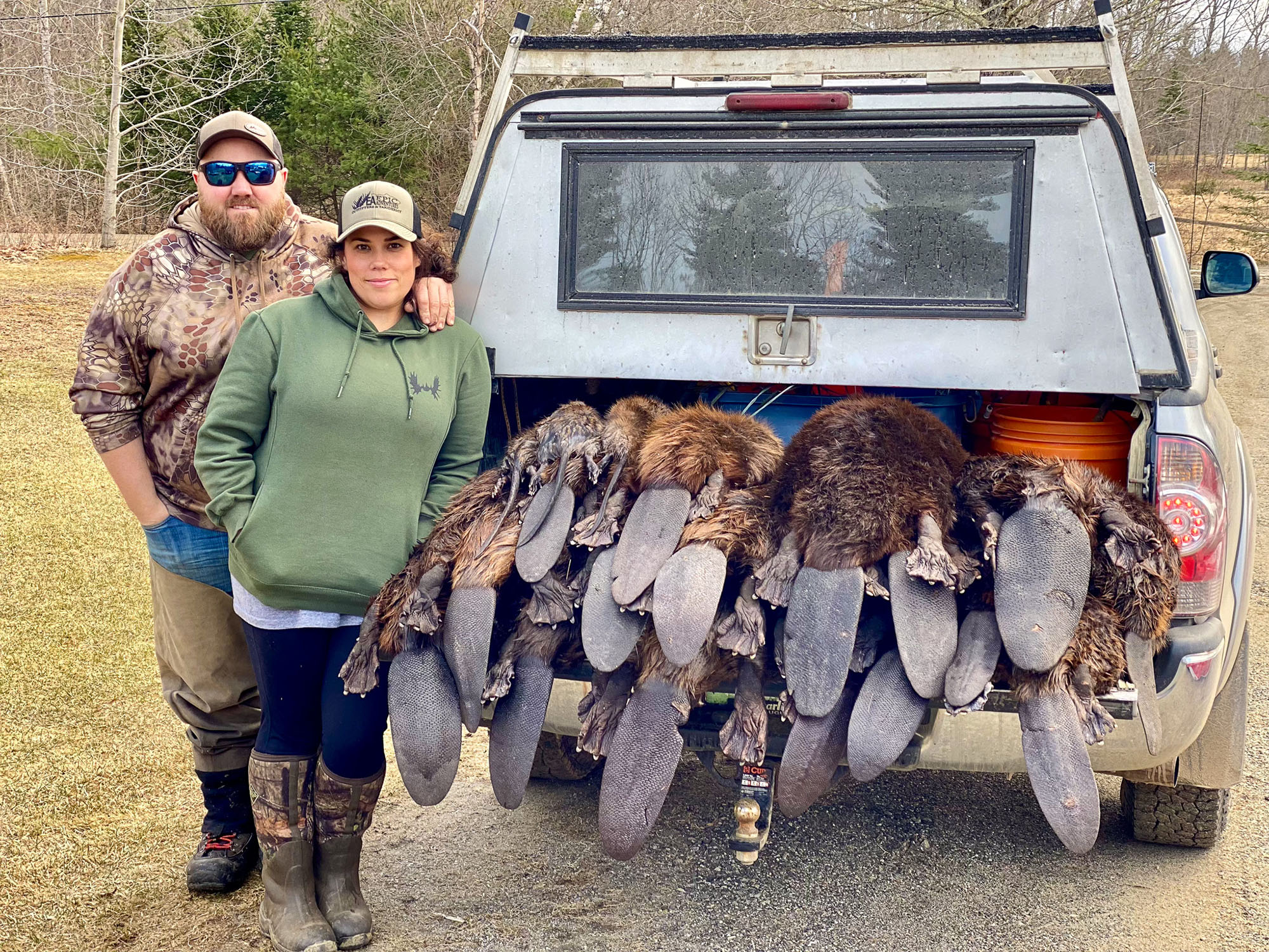 Two trappers stand by a truck tailgate with beavers on it.