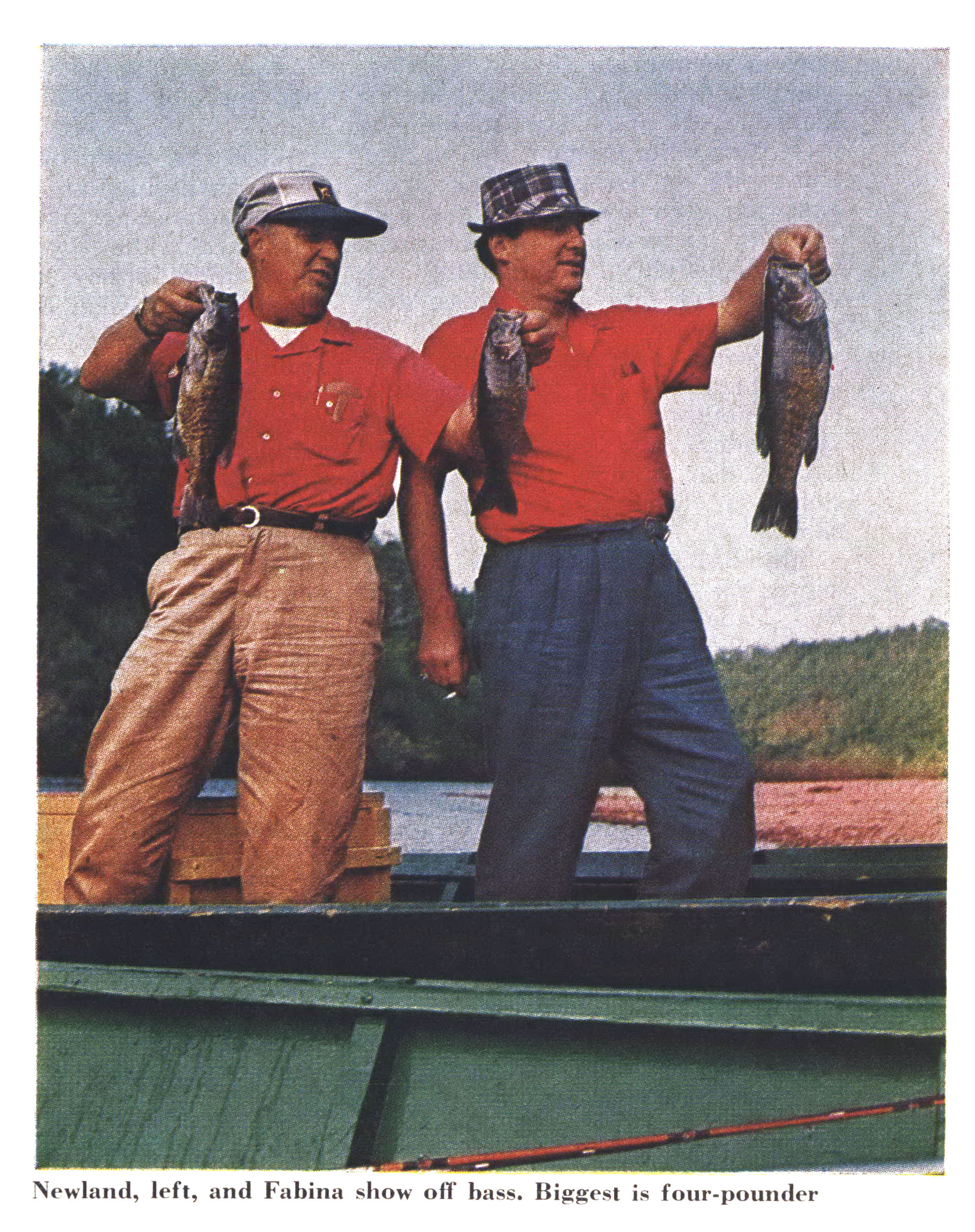 An old color photograph of two men in red shirts holding up bass while standing in a boat.