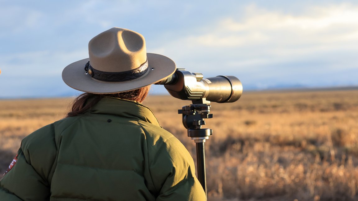 A National Park Service ranger looks through a spotting scope.