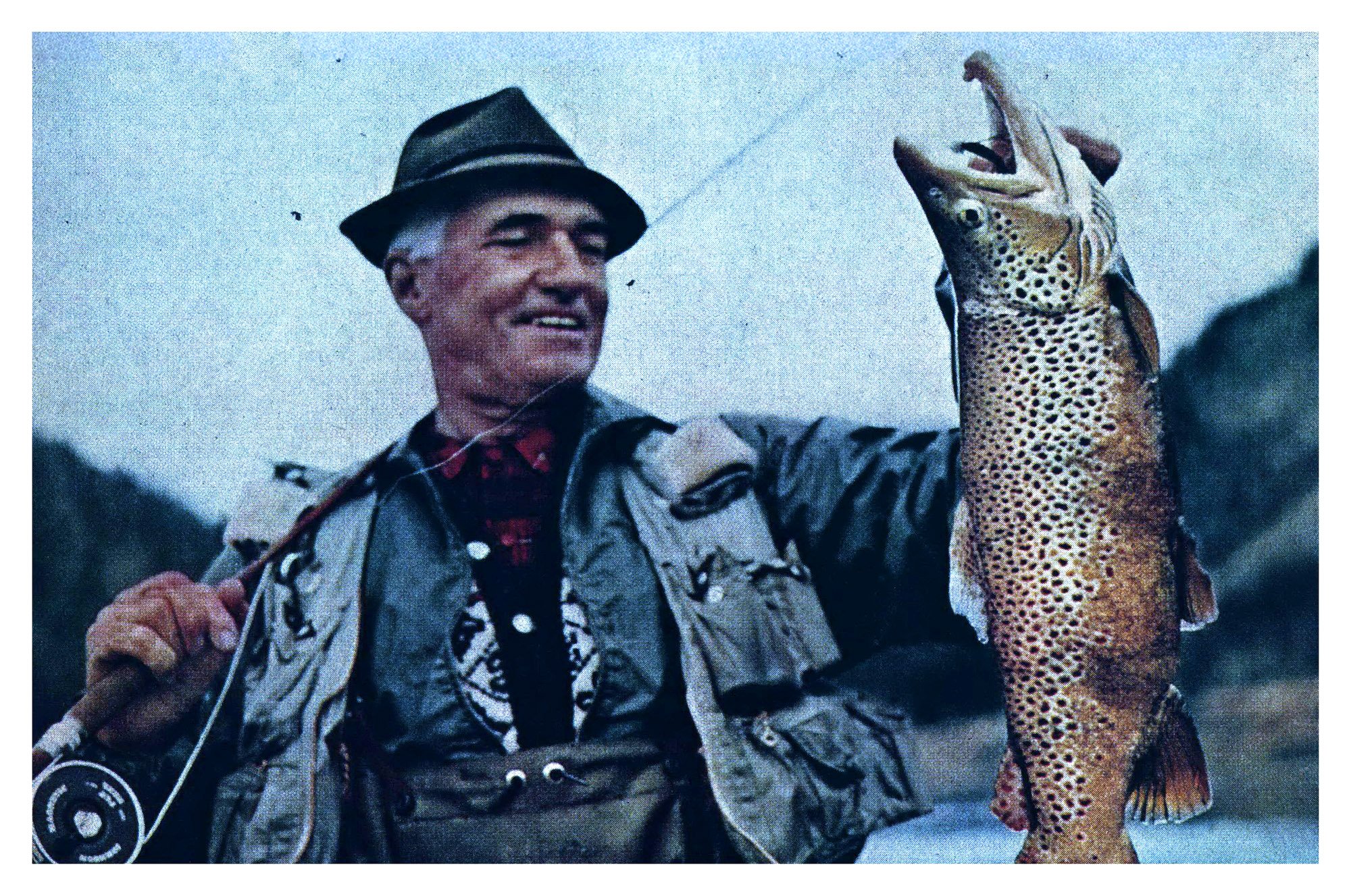 A color film photograph of a man holding up a giant trout.