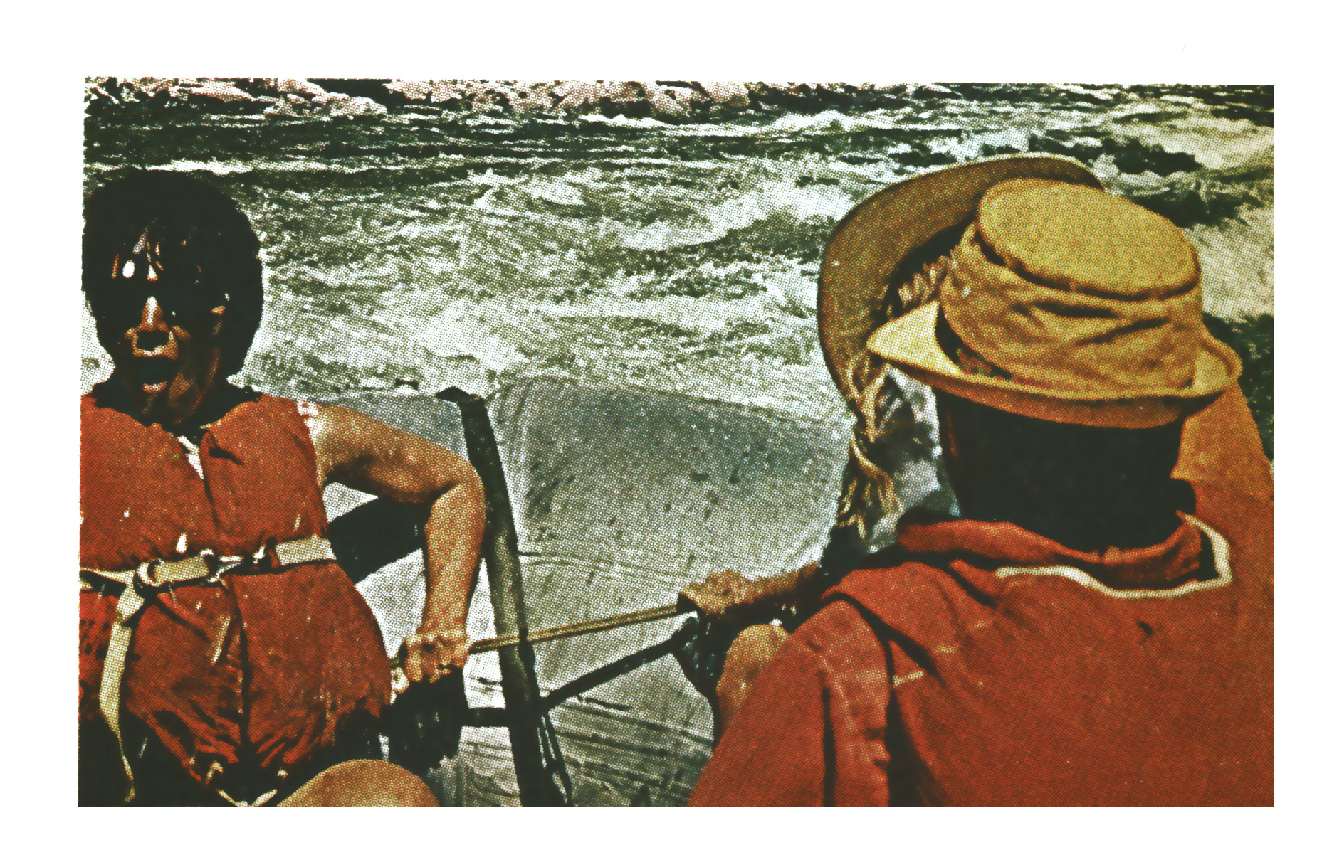 Two rafters in red life jackets and brimmed hats row toward rough whitewater, seen from behind aboard the raft.