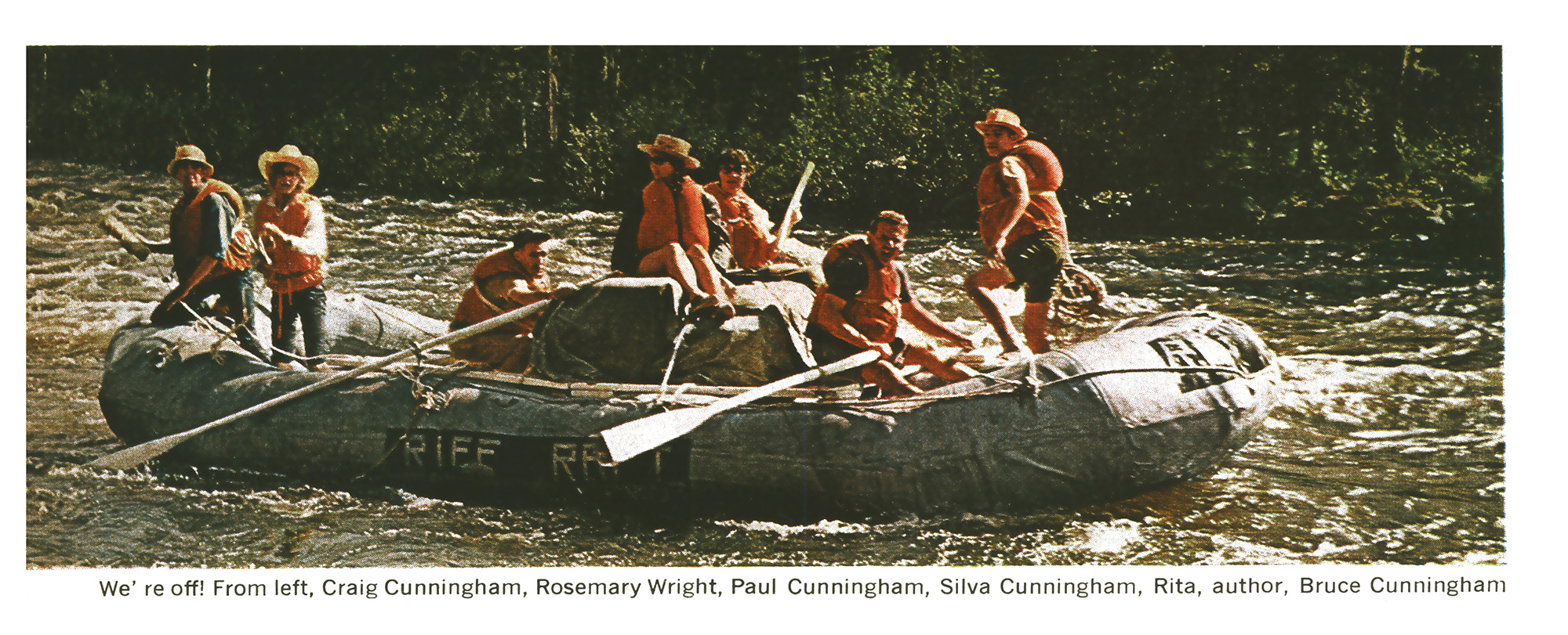 A large gray pontoon raft crowded with the trip party, in life vests and hats, pushing off into a calm stretch of river lined with forest.