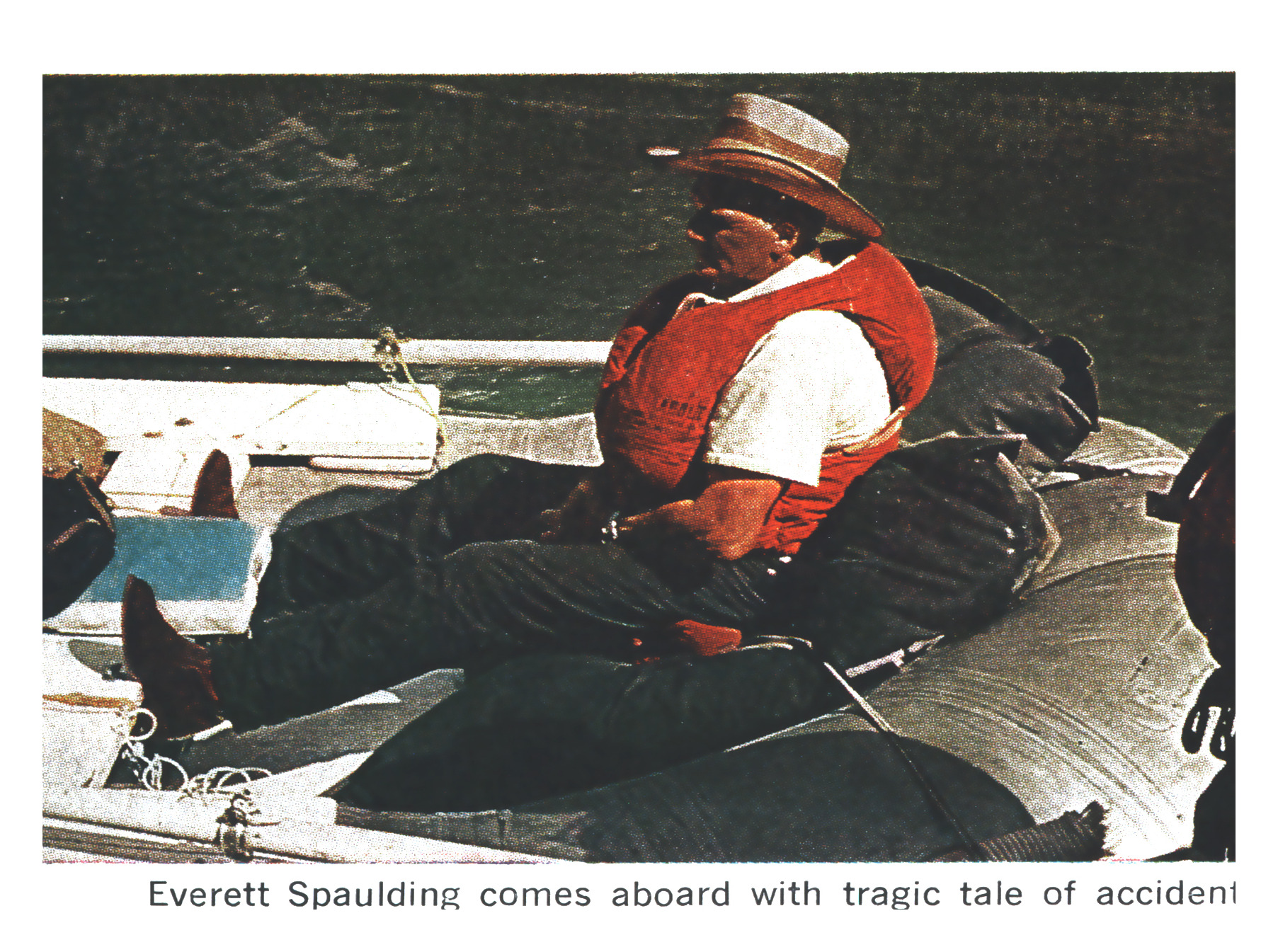 A man in a straw hat, red life vest, and white shirt sits aboard a gear-laden raft on dark water.