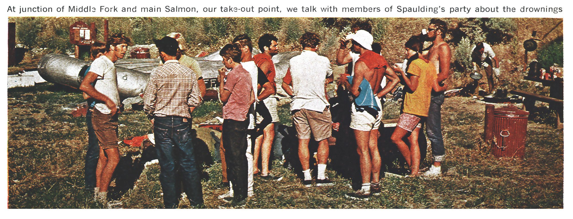 A crowd of young people in shorts and life vests gathers on a grassy bank beside rafts at the river take-out point.