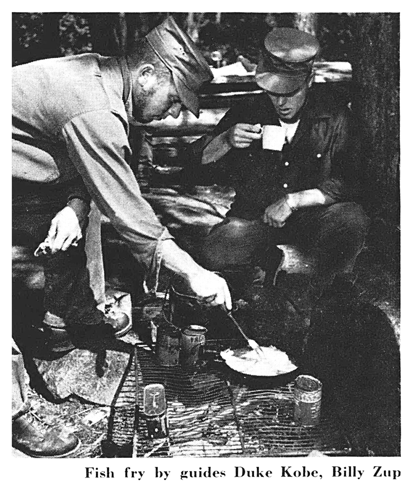 Guides Duke Kobe and Billy Zup cook a shore-lunch fish fry over a camp stove on the rocks (black-and-white photo).