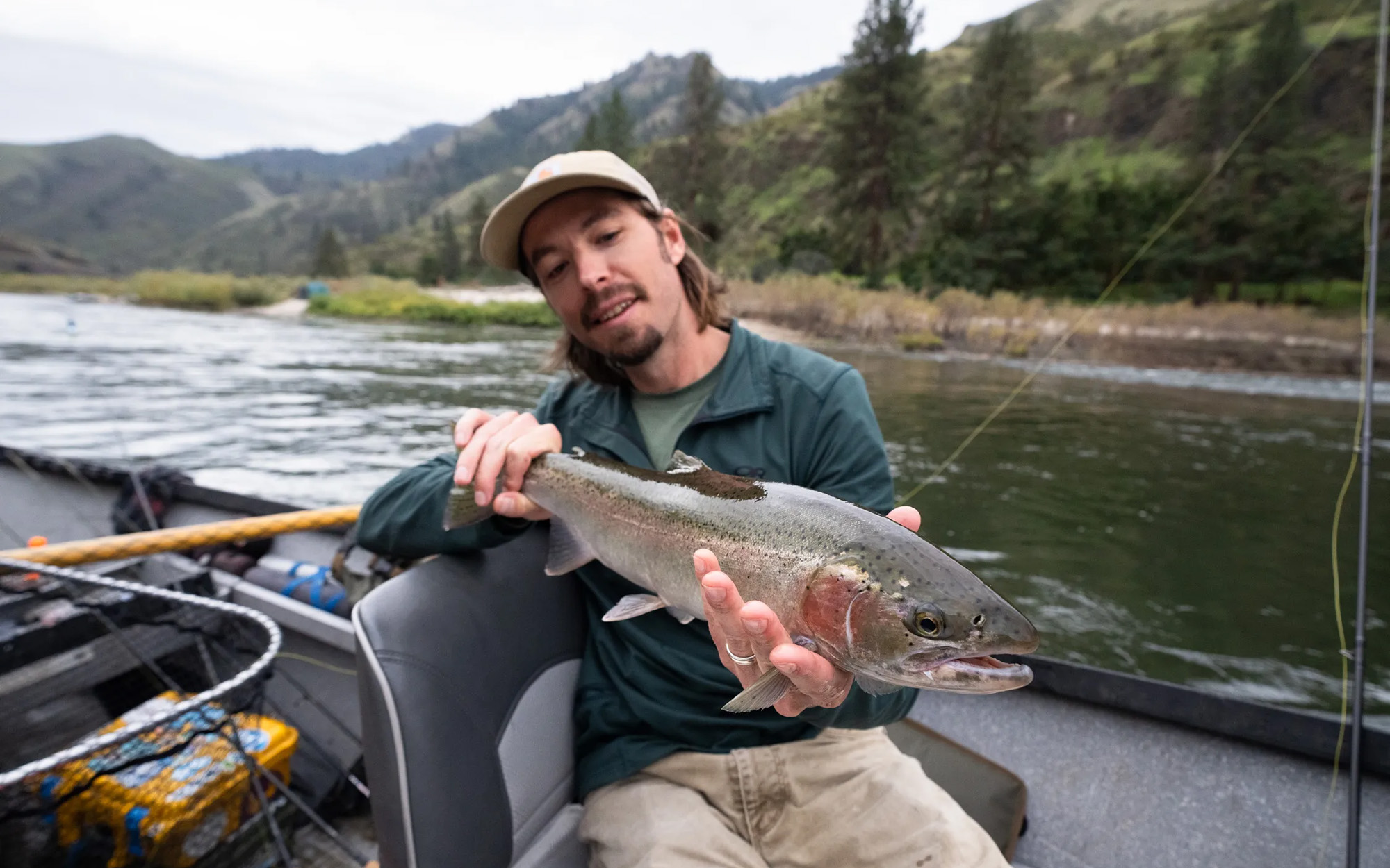 A fisherman in a drift boat catches a steelhead.