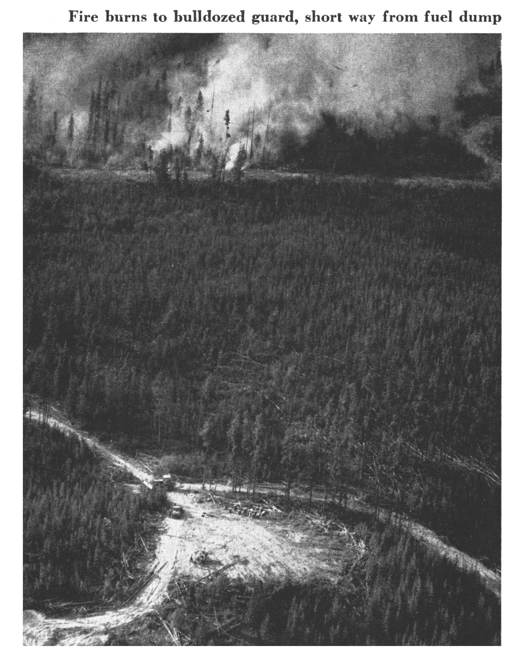 An old black and white photo of a bulldozer fire break as a wildfire rages.