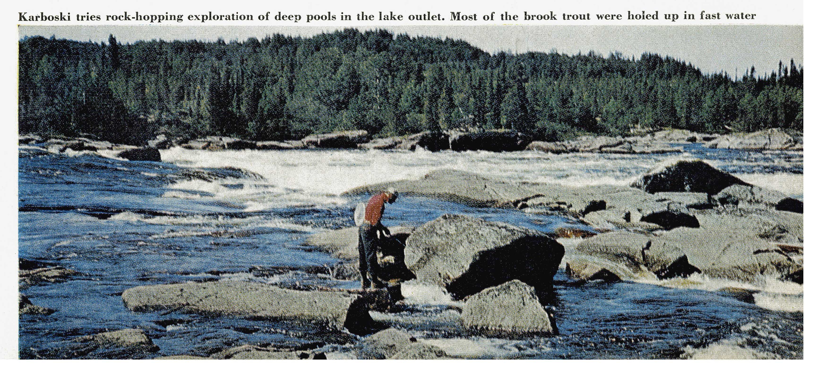 A lone angler fishes among rocks in fast, foaming water of the lake outlet rapids, backed by dense forest.