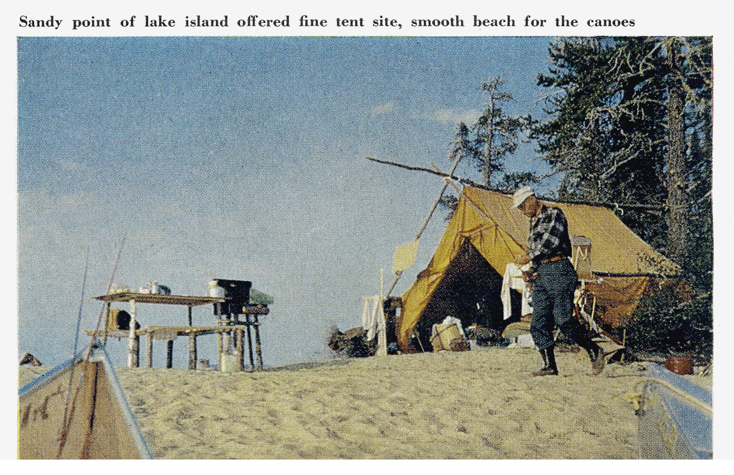 A wall tent and camp gear set up on the sandy point of a wooded lake island, with canoes beached nearby.