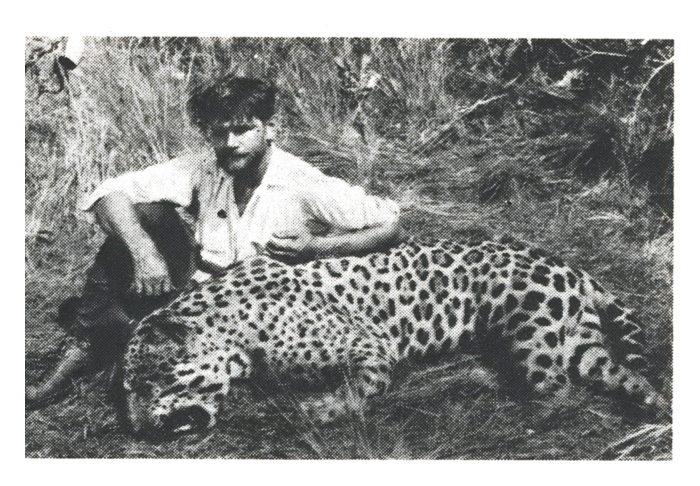 Black-and-white photo of a young Sasha Siemel kneeling in tall grass beside a dead jaguar.