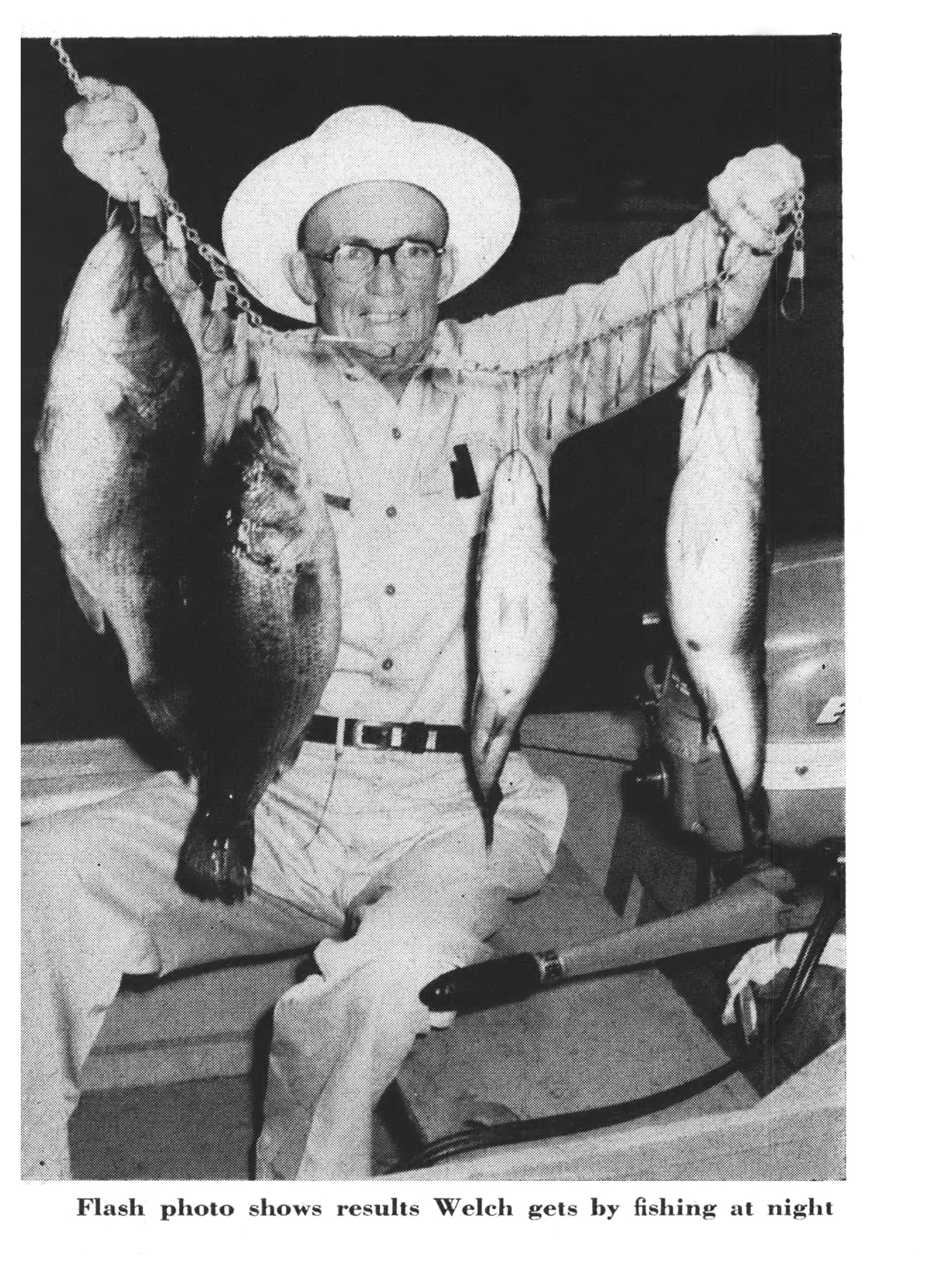 Nighttime flash photo of Sam Welch seated in a boat, holding up two big bass on separate stringers.