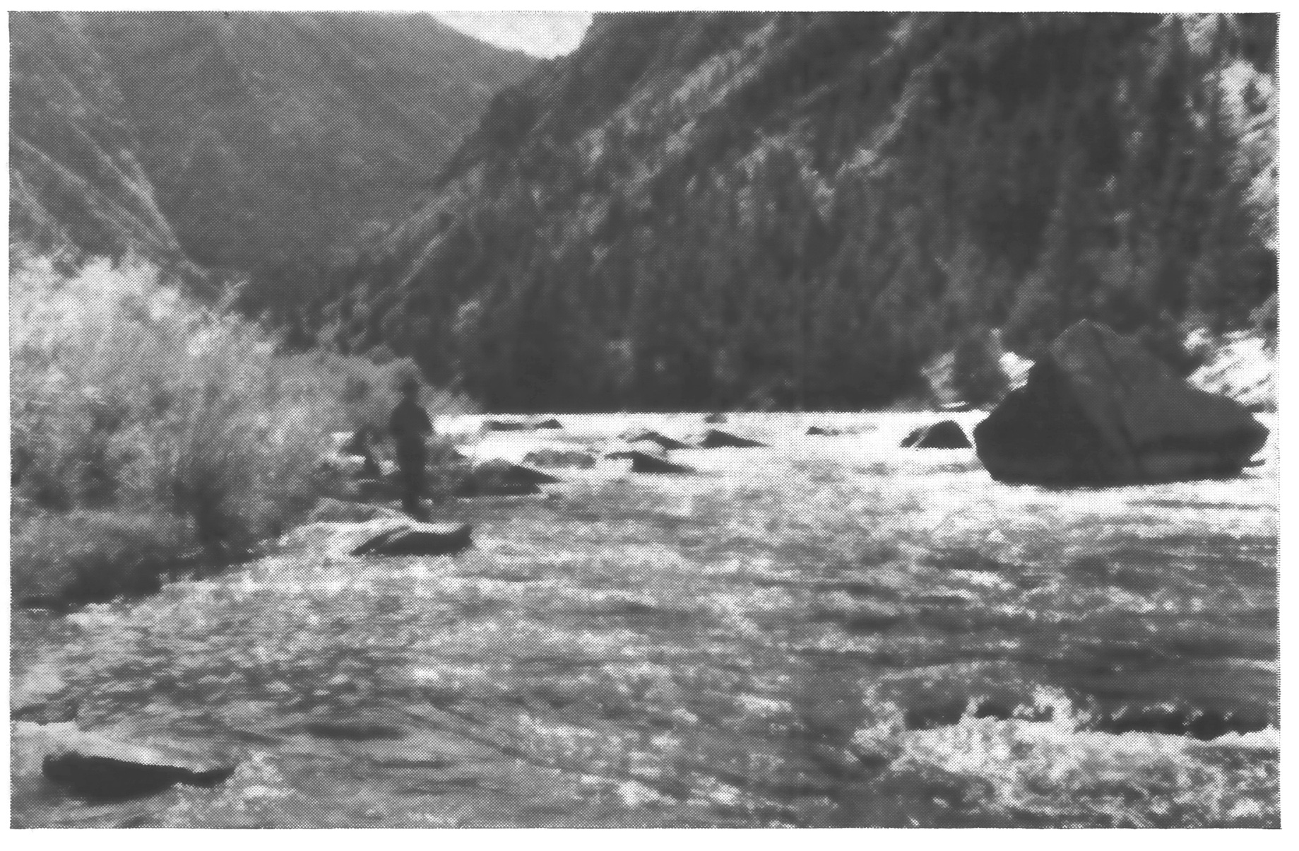 Black-and-white photo of a lone angler fishing Montana's Madison River amid boulders in a steep canyon.