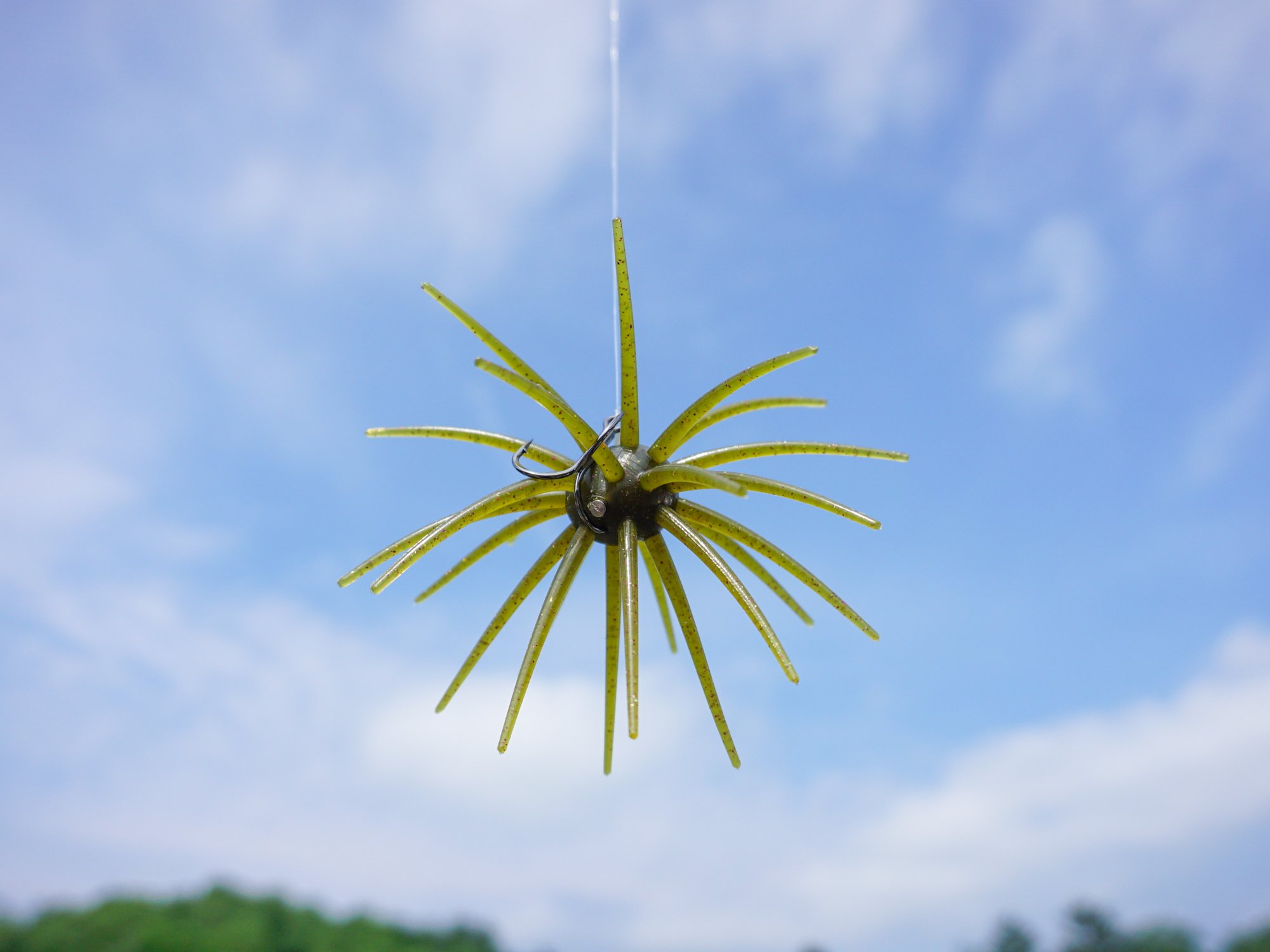 A green urchin bass bait against a blue sky with some clouds.