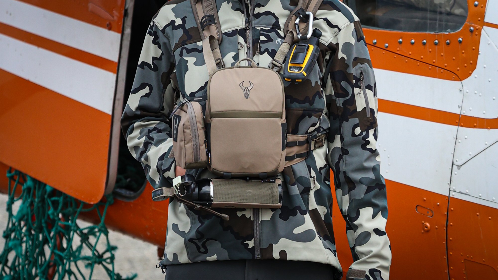 A hunter wearing kuiu camo and a bino harness has a holstered can of bear spray.