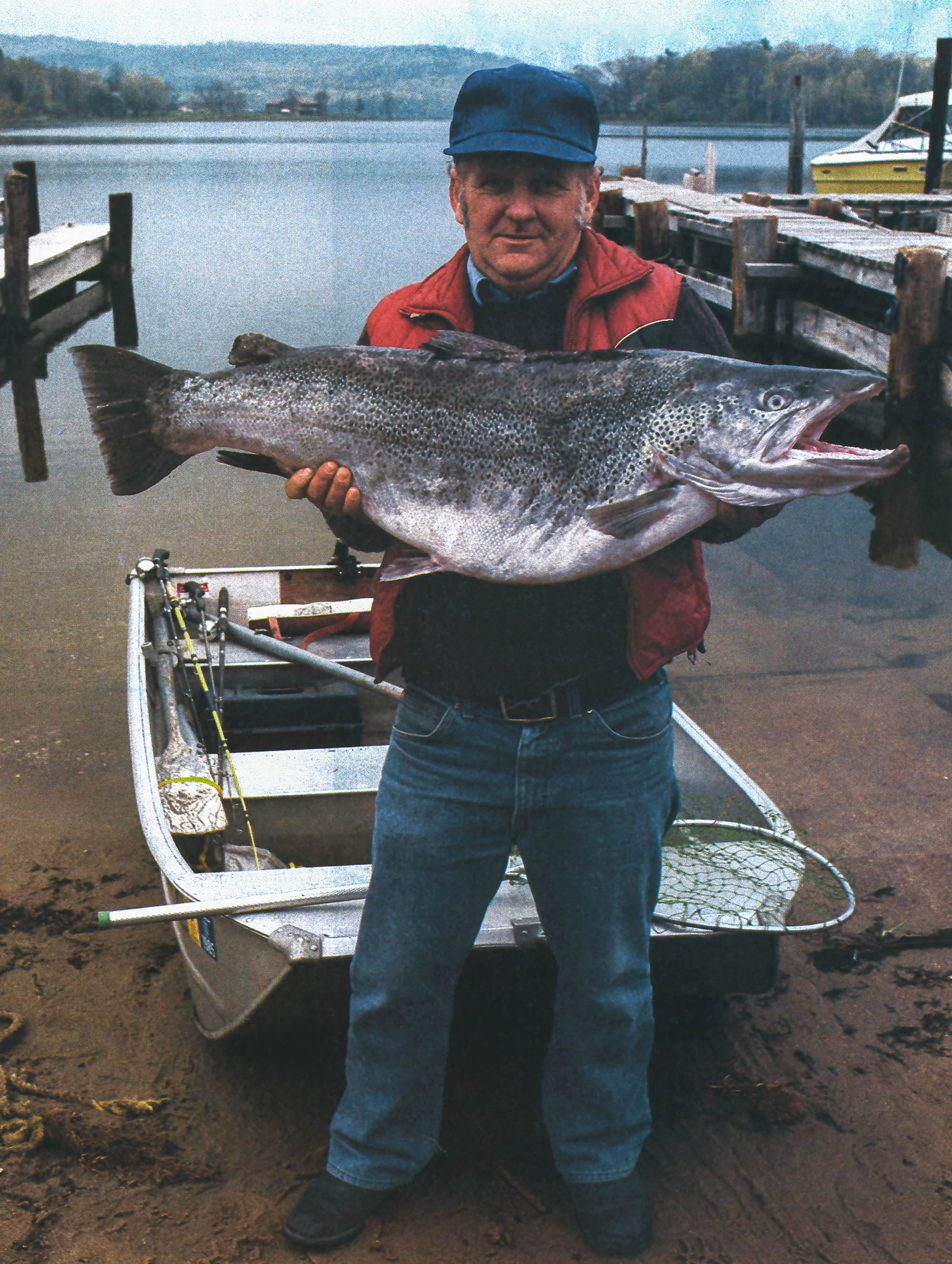A vertical photo of Bob Henderson holding up an enormous record brown trout.