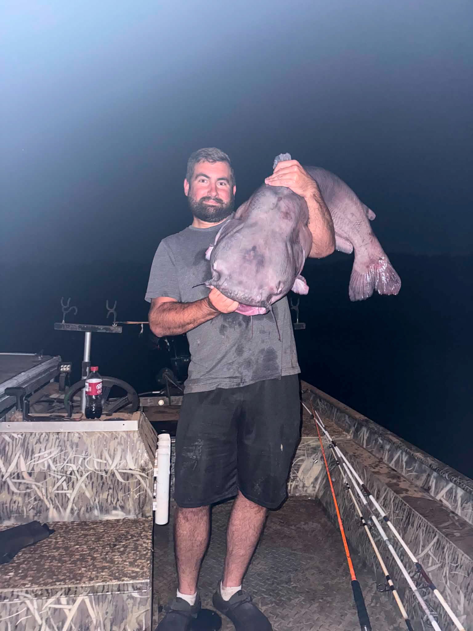 A man holds up a big blue catfish over his shoulder.