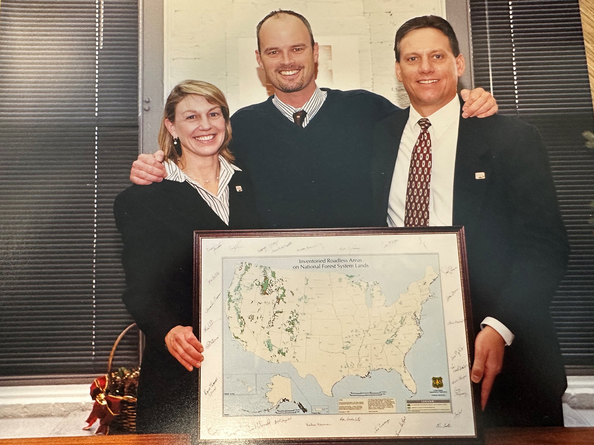 A photo of Chris Wood, Julia Riber, and Scott Conroy holding a framed map of inventoried roadless areas.