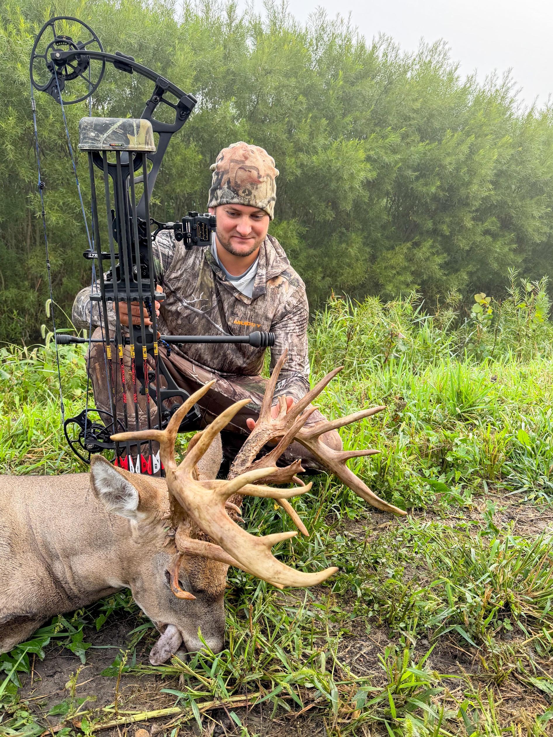 A vertical photo of a bowhunter admiring a big Ohio buck.