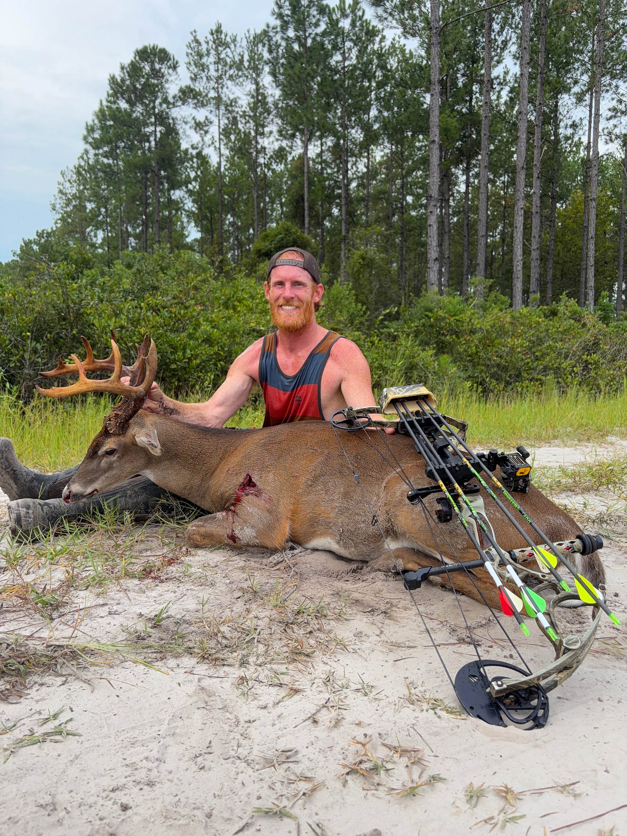 A florida bowhunter sits behind a deer in the sand.