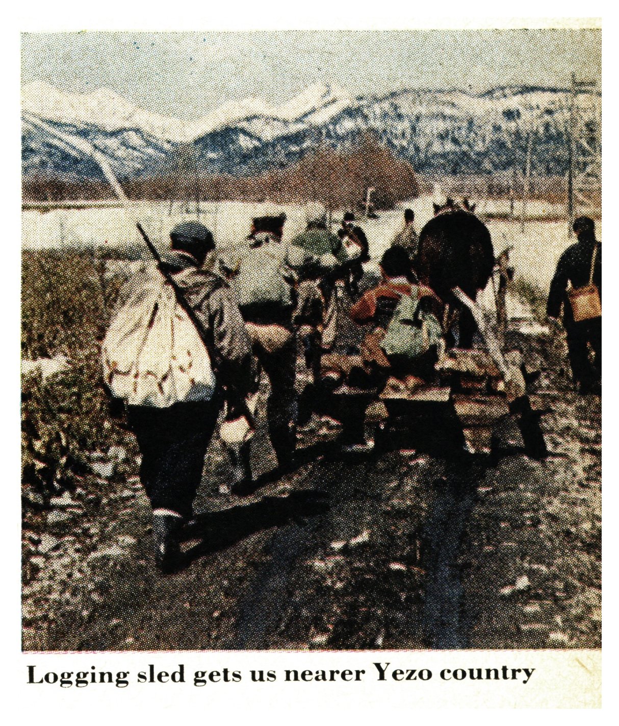 A group of men in winter gear walk alongside a loaded logging sled on a snow-edged track, with snow-covered mountains behind them.