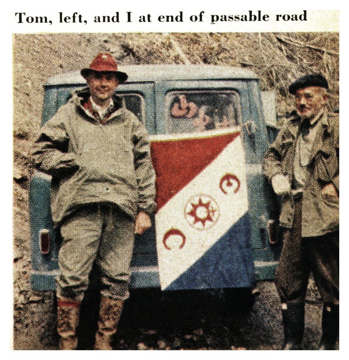 Two men in hunting clothes stand at the back of a small van at the end of a dirt road, beside a triangular expedition pennant.