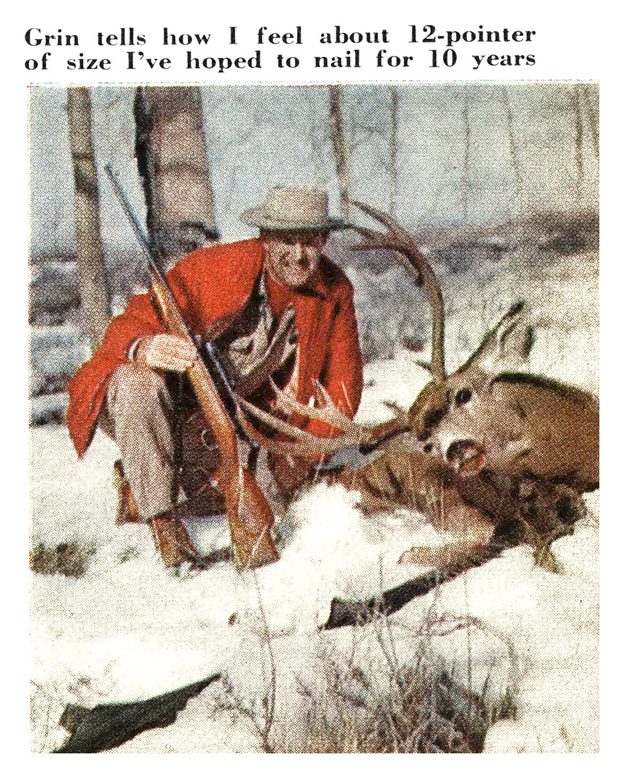 A smiling hunter in a red jacket and brimmed hat kneels with his rifle beside a large mule deer buck in the snow.