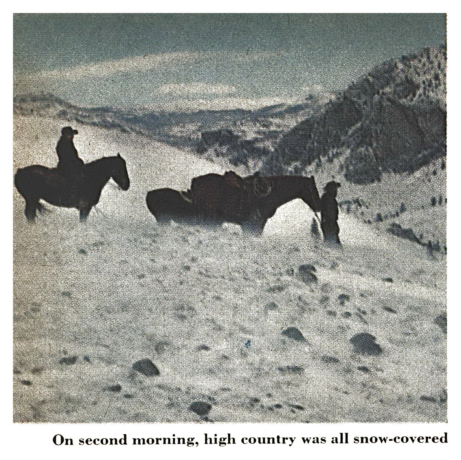 Two hunters and their horses on a windswept, snow-covered mountainside with rugged peaks and a valley behind them in Wyoming's Wind River country.