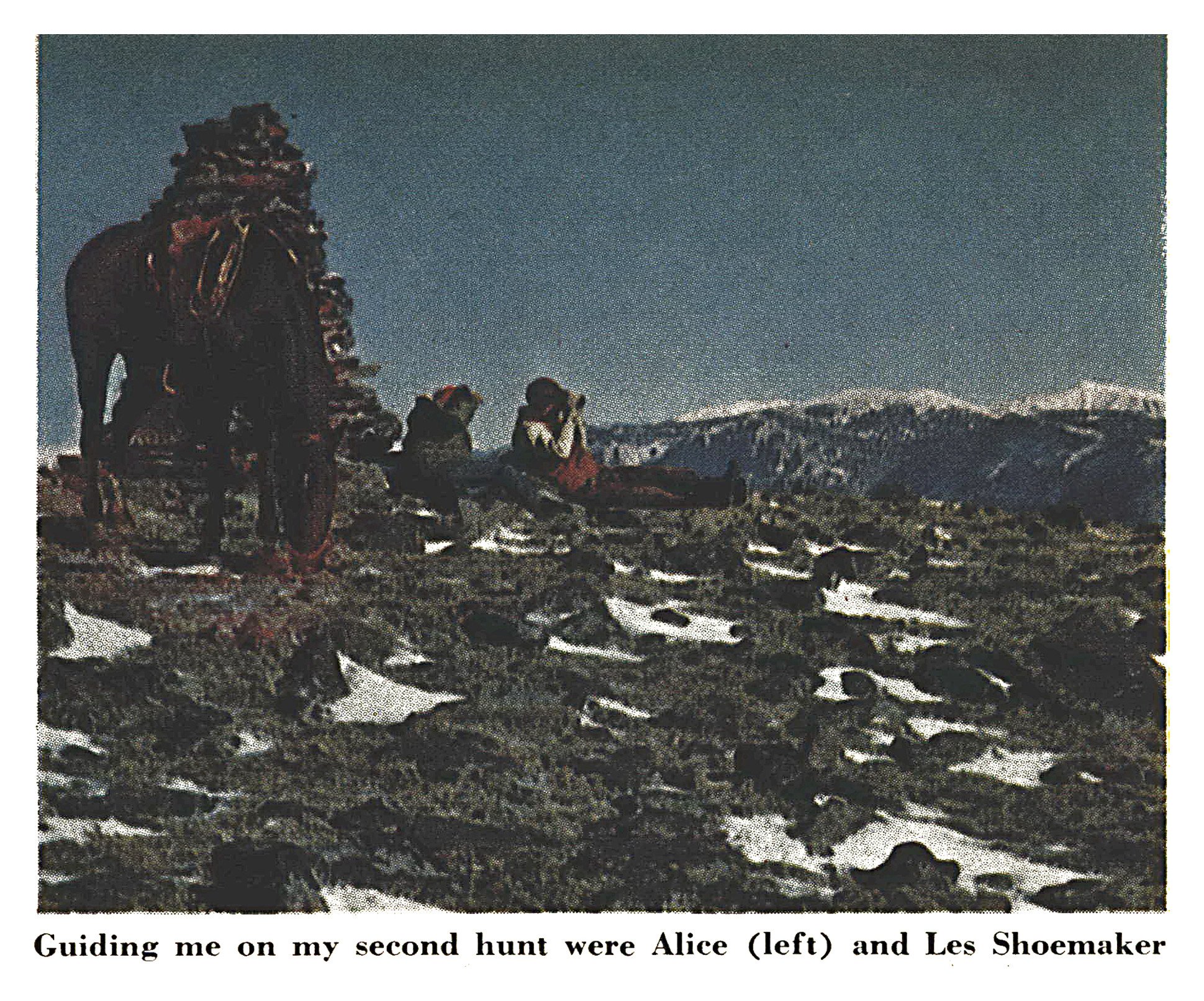 A packhorse stands beside a tall stone cairn while two outfitters sit glassing a high, snow-patched mesa with snowcapped mountains in the distance.
