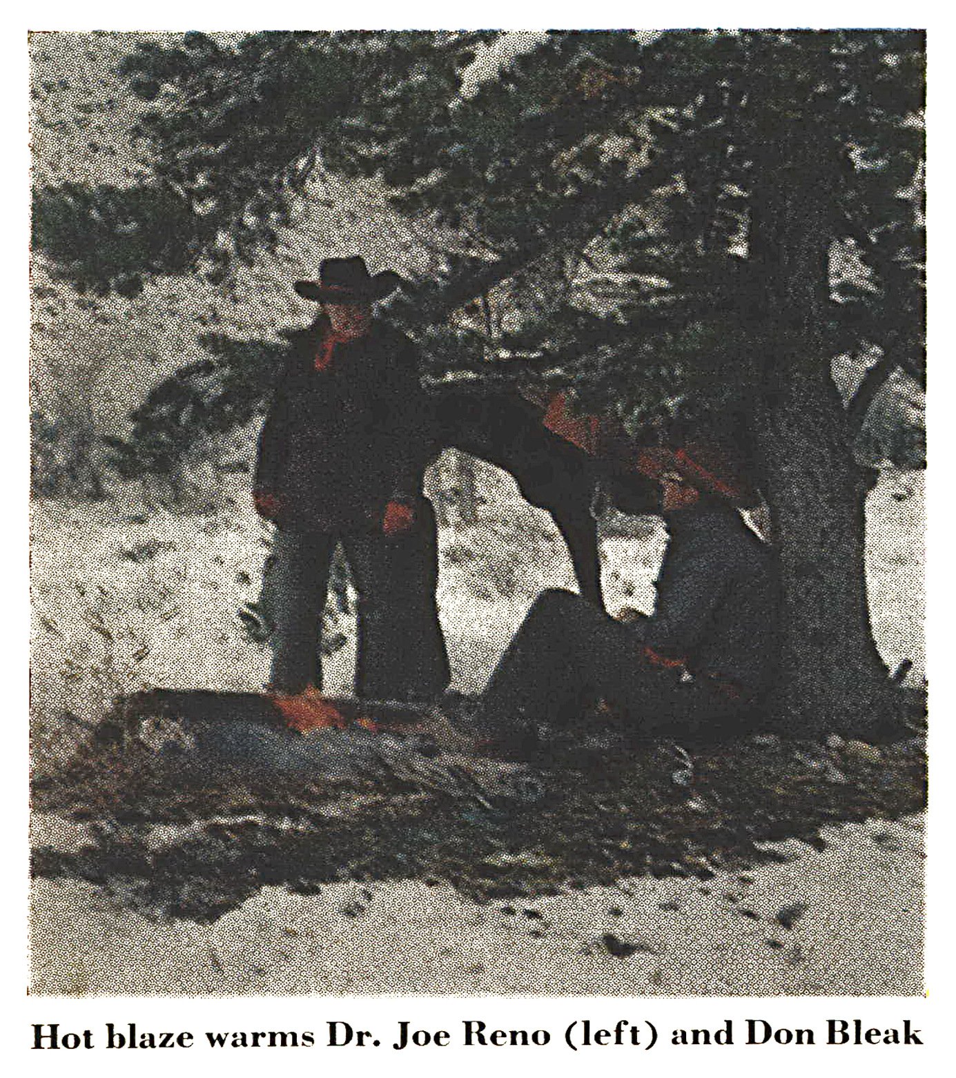 Two hunters in cowboy hats warm themselves at a small fire beneath a large pine tree, with a saddled horse behind them and snow on the ground.